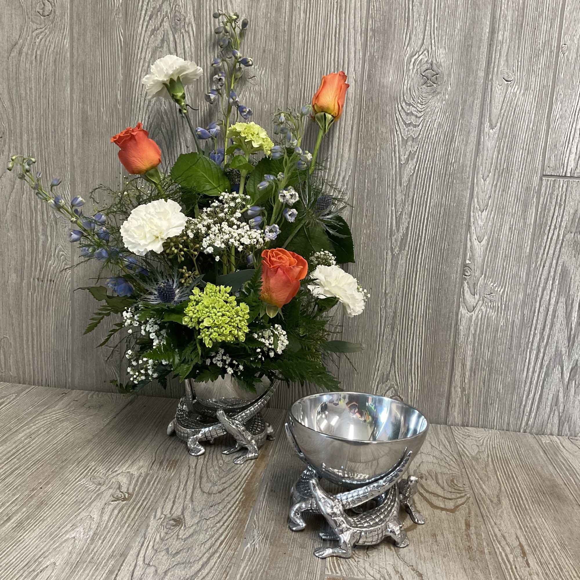 Bright orange roses set against soft blue delphinium, crisp white carnations, and