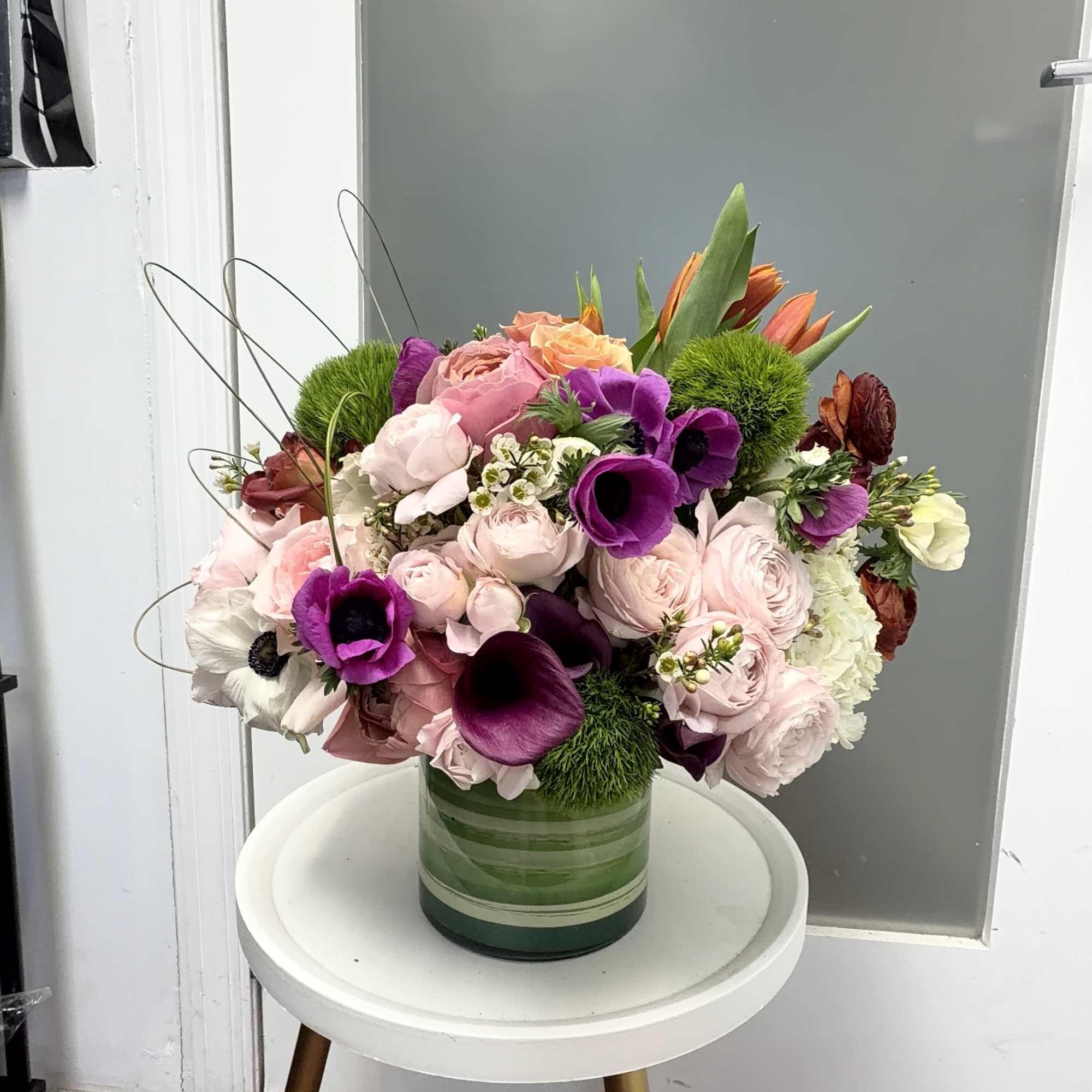 Mixed bouquet of pink, purple, white, and orange flowers in a green glass vase