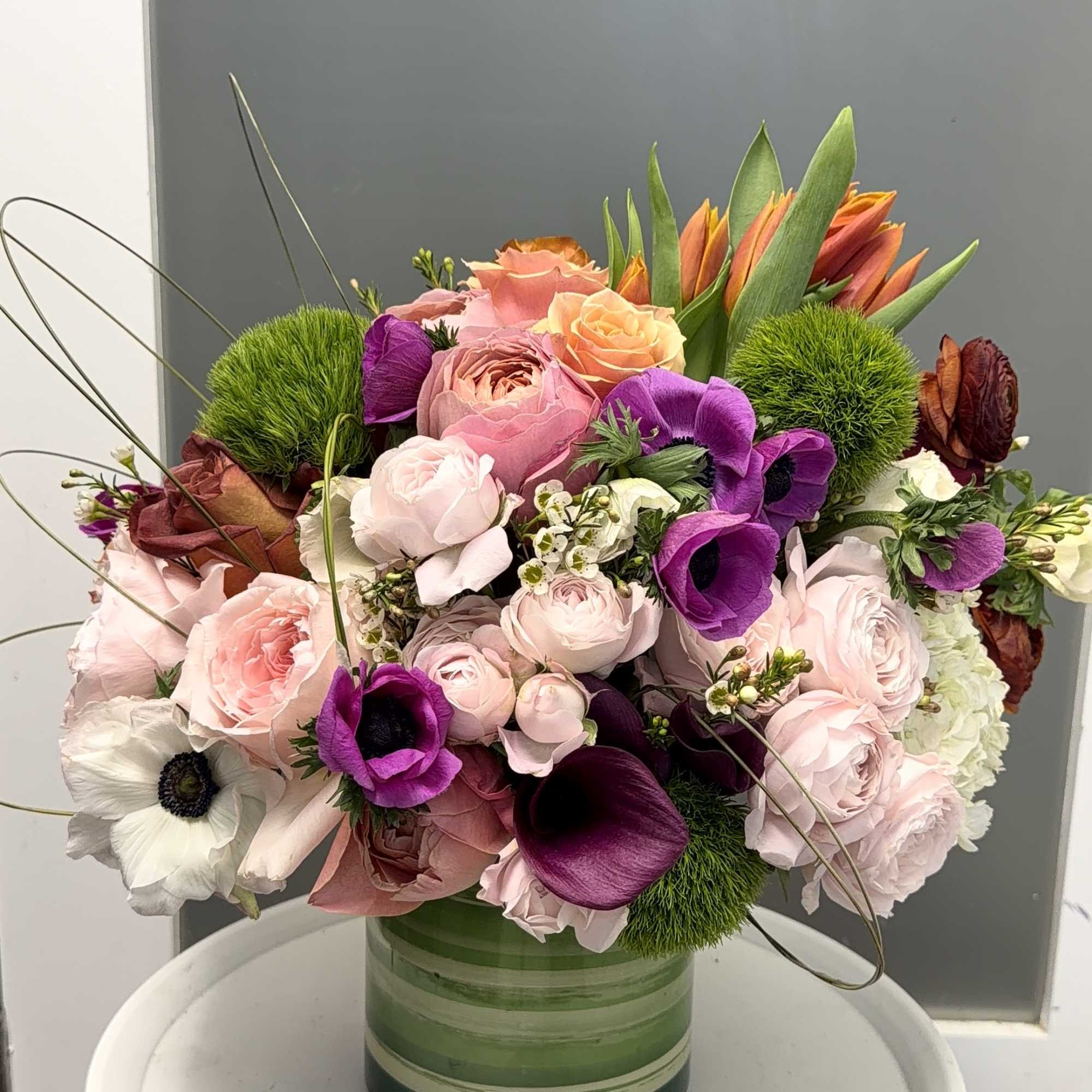Mixed pink, purple, and orange flowers arranged in a green glass vase.