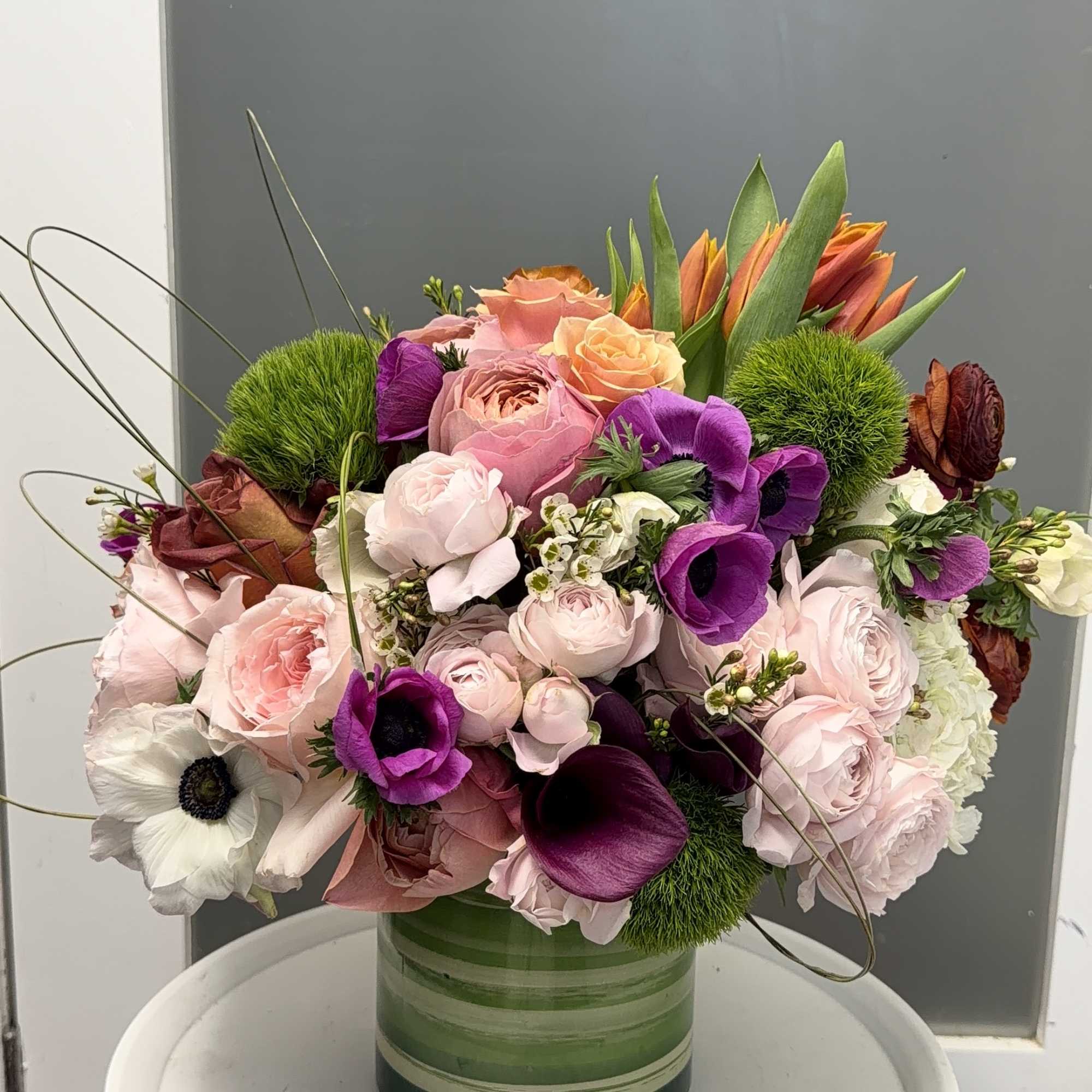 Mixed bouquet of pink, purple, white, and orange flowers in a green striped vase