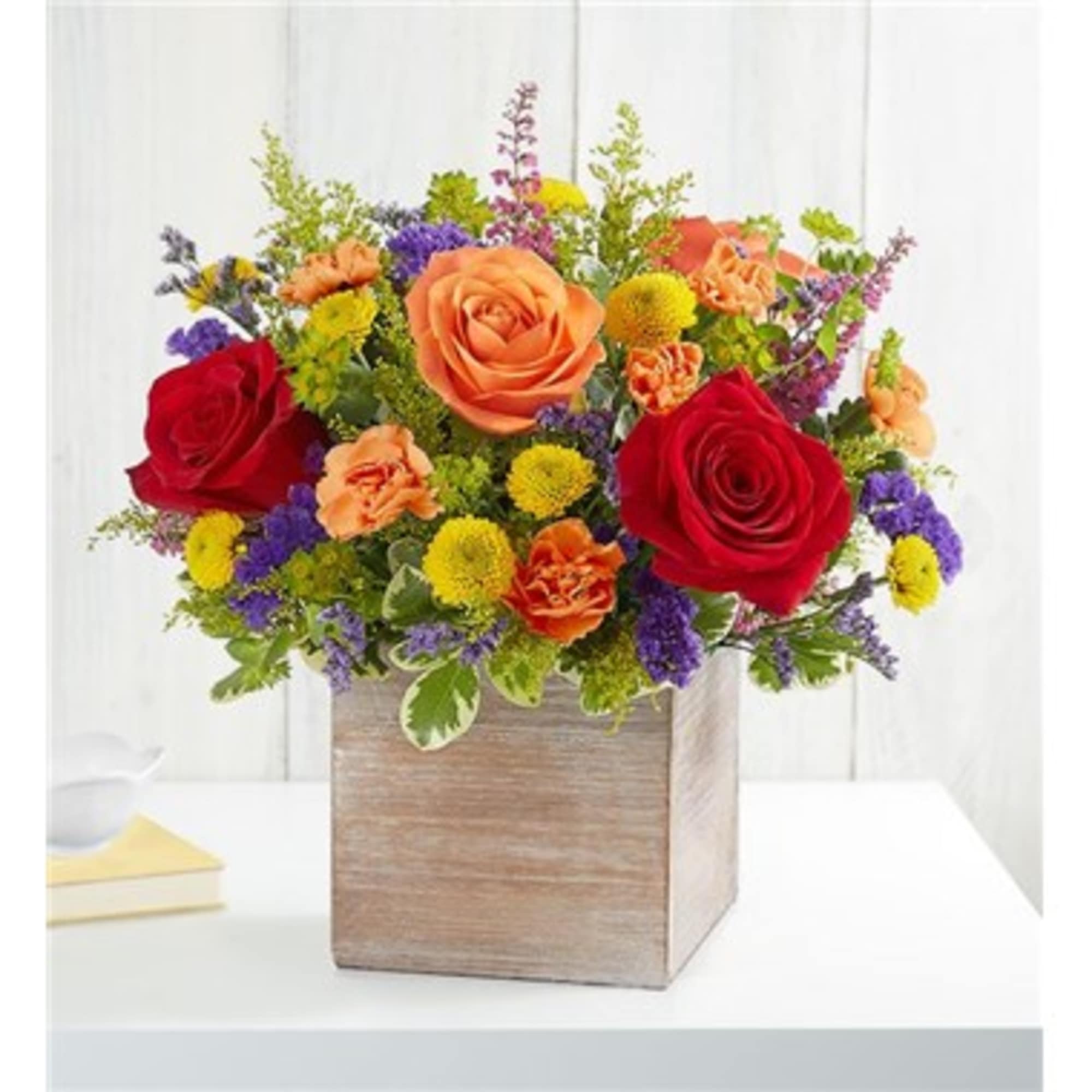 Mixed bouquet of roses, carnations, and small purple and yellow flowers in a wooden box