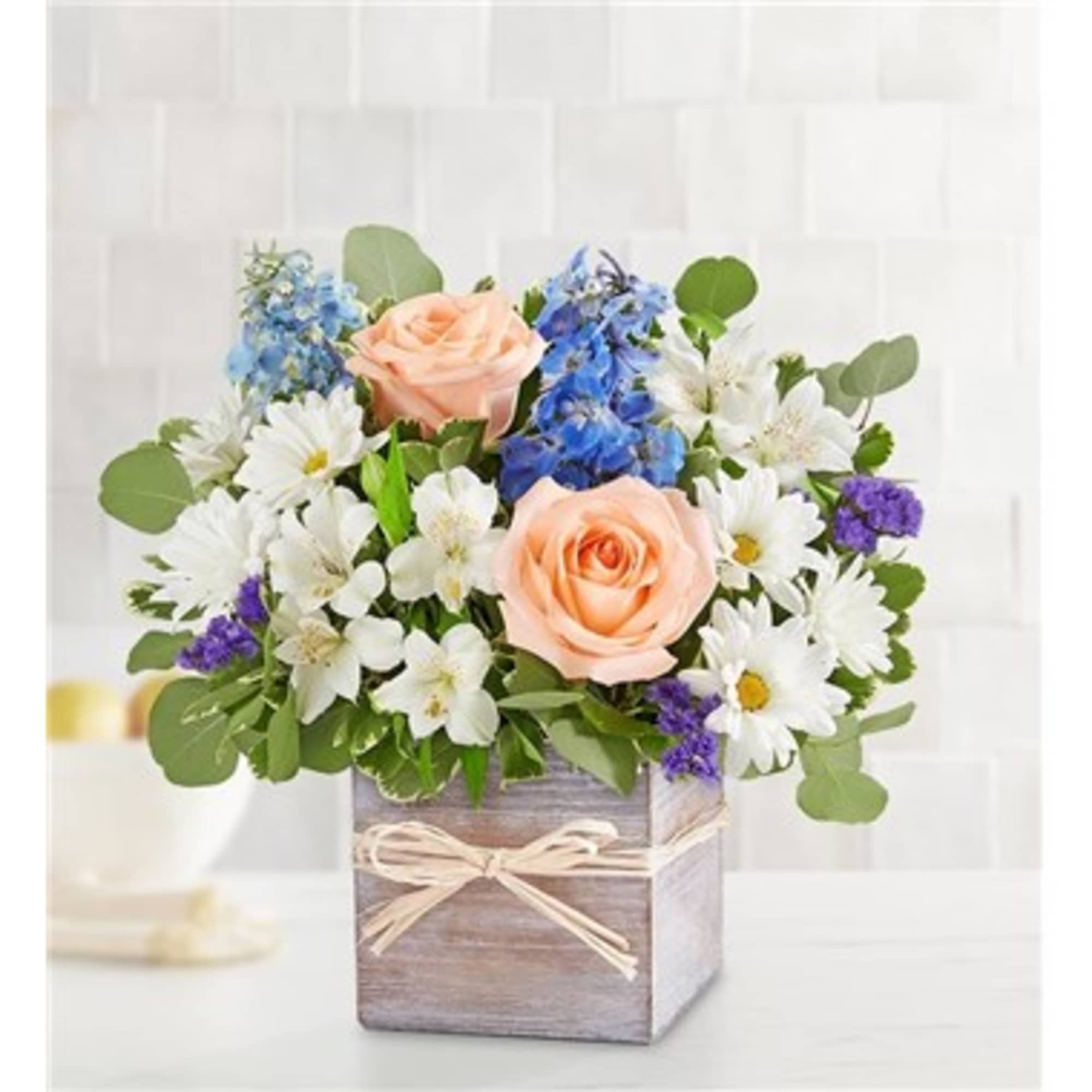 Peach roses and white daisies in a wooden box with blue flowers