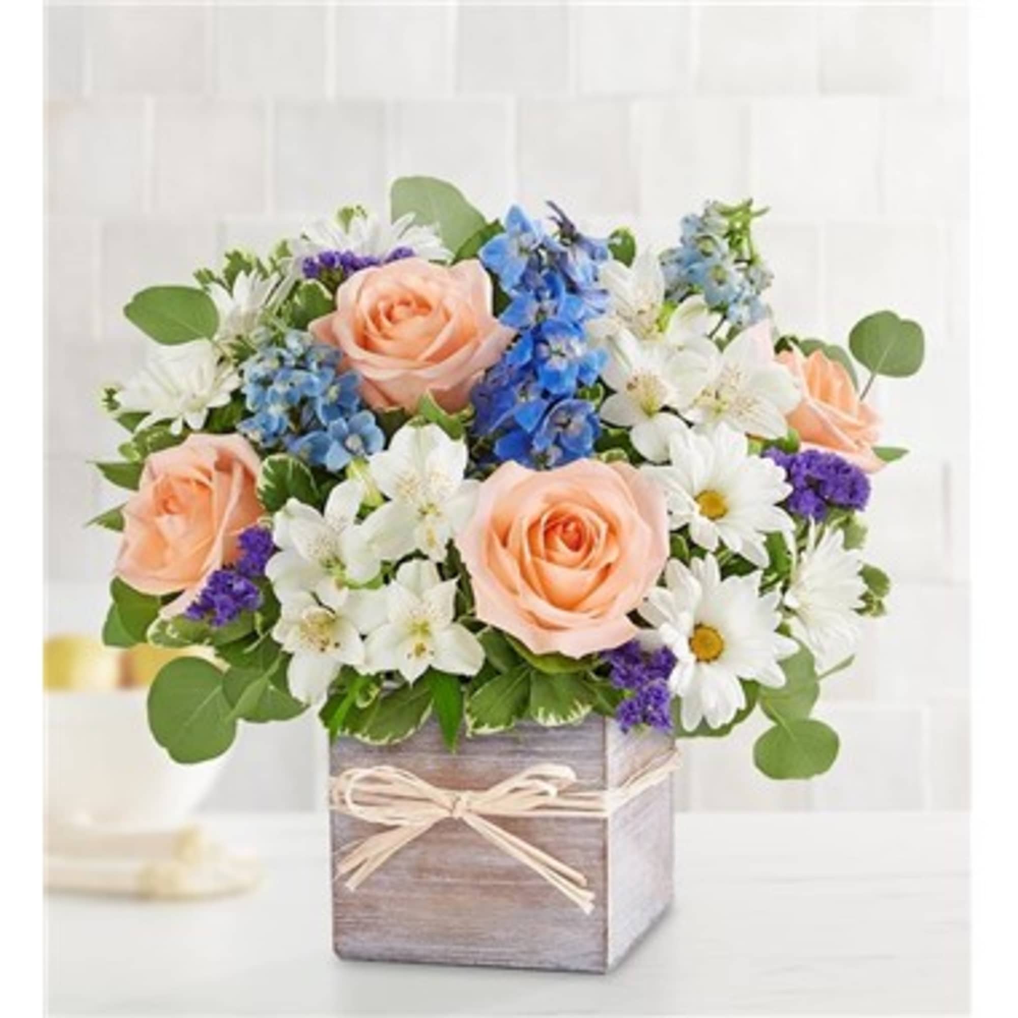 Mixed bouquet of peach roses, white daisies, and blue flowers in a wooden box
