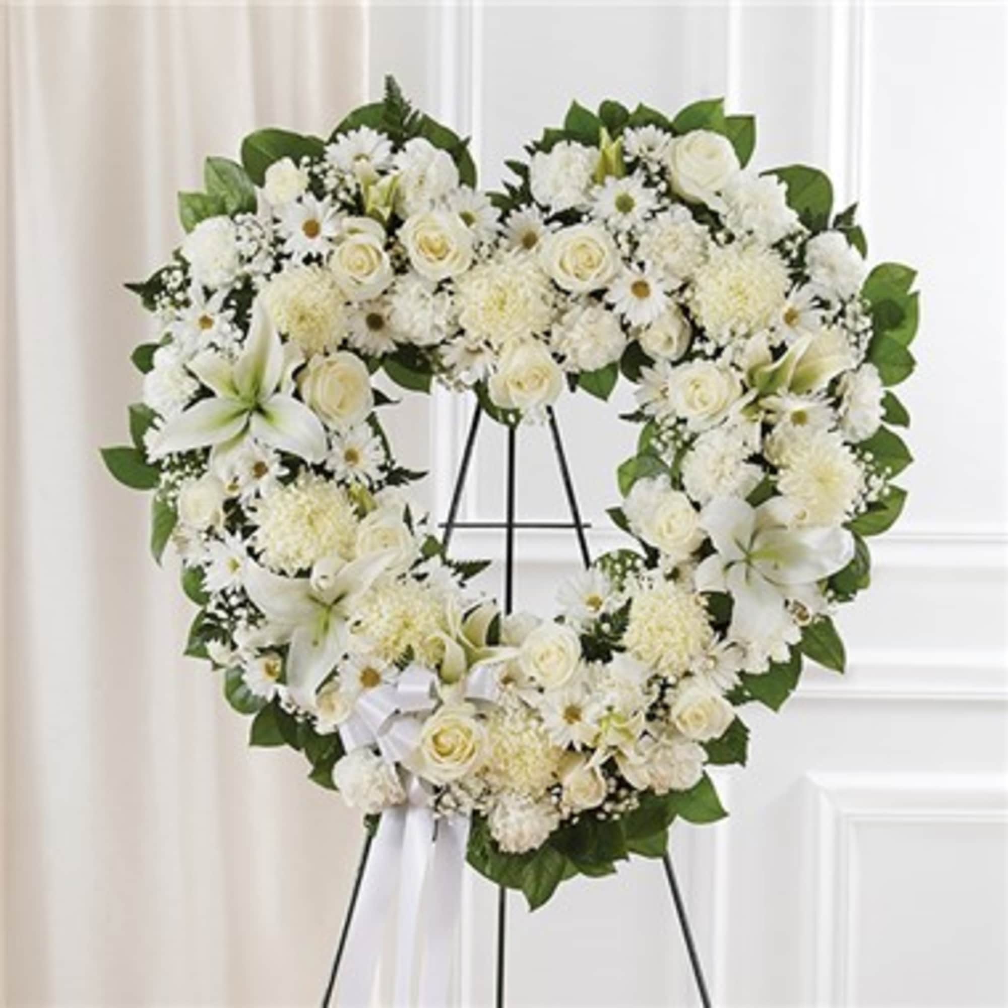 Heart-shaped white floral wreath on a stand with a white ribbon