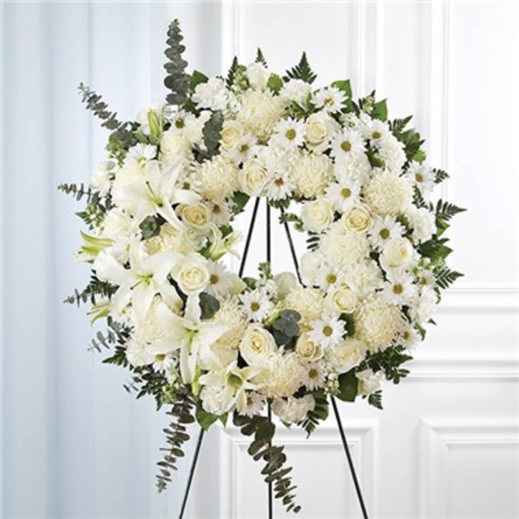 White floral wreath on a black stand with roses and daisies