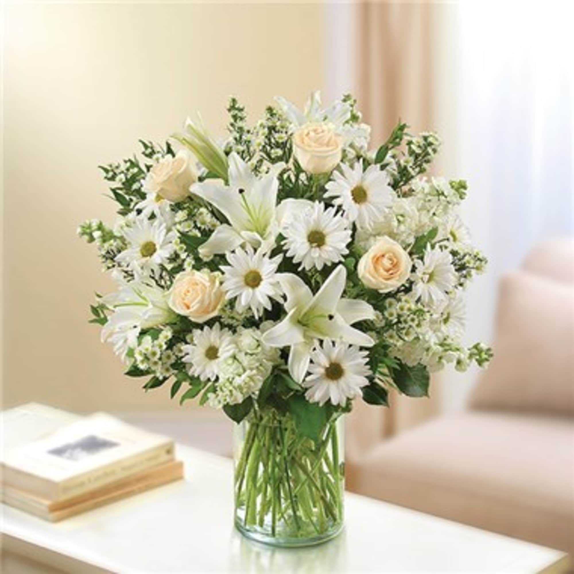 White lilies, daisies, and pale roses in a clear glass vase