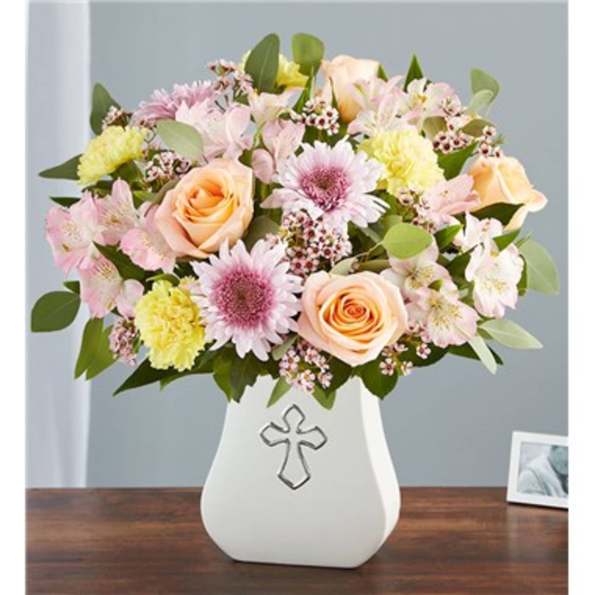 Pastel mixed flower arrangement in a white vase with a cross emblem