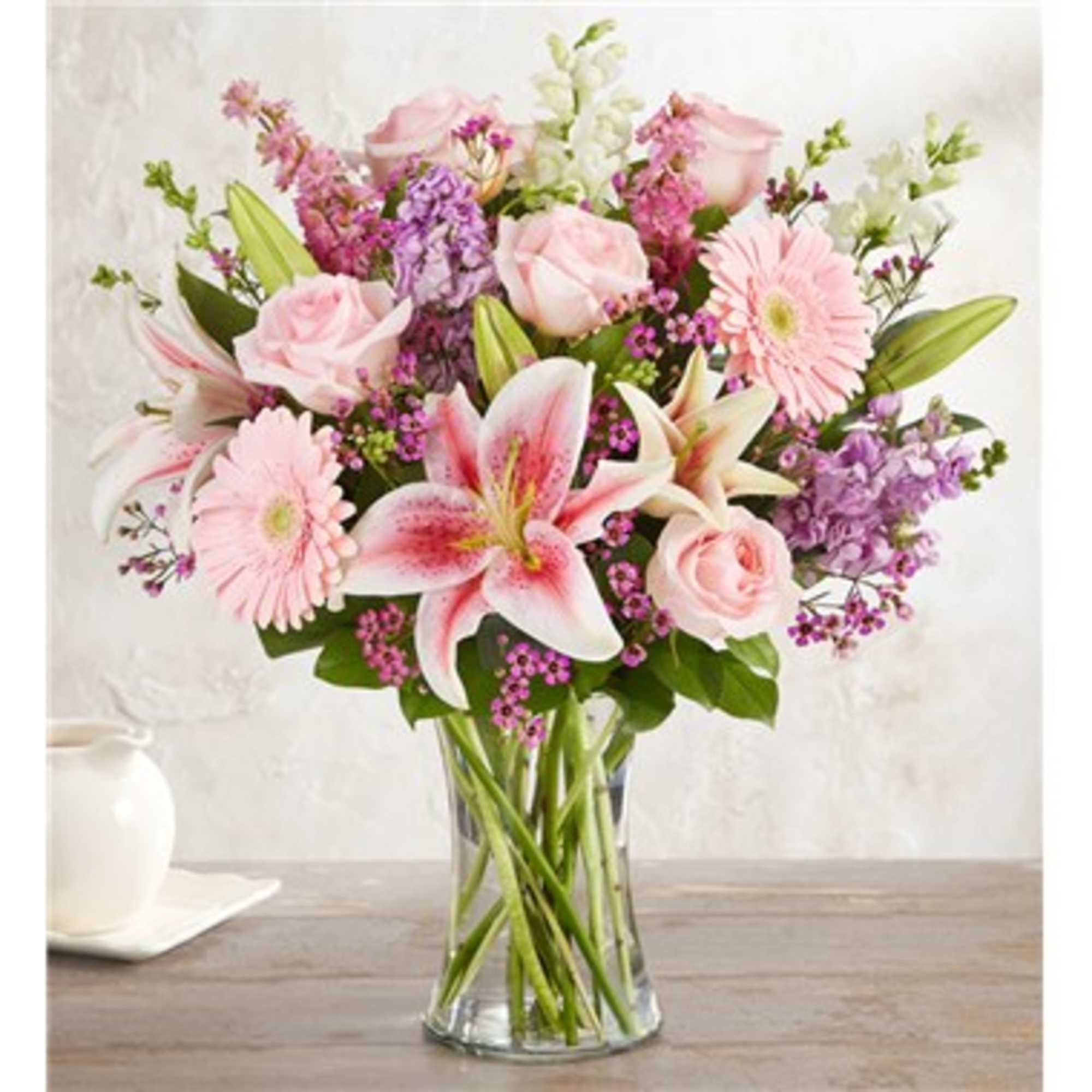 Mixed bouquet of pink lilies, roses, gerbera daisies and purple flowers in a clear glass vase