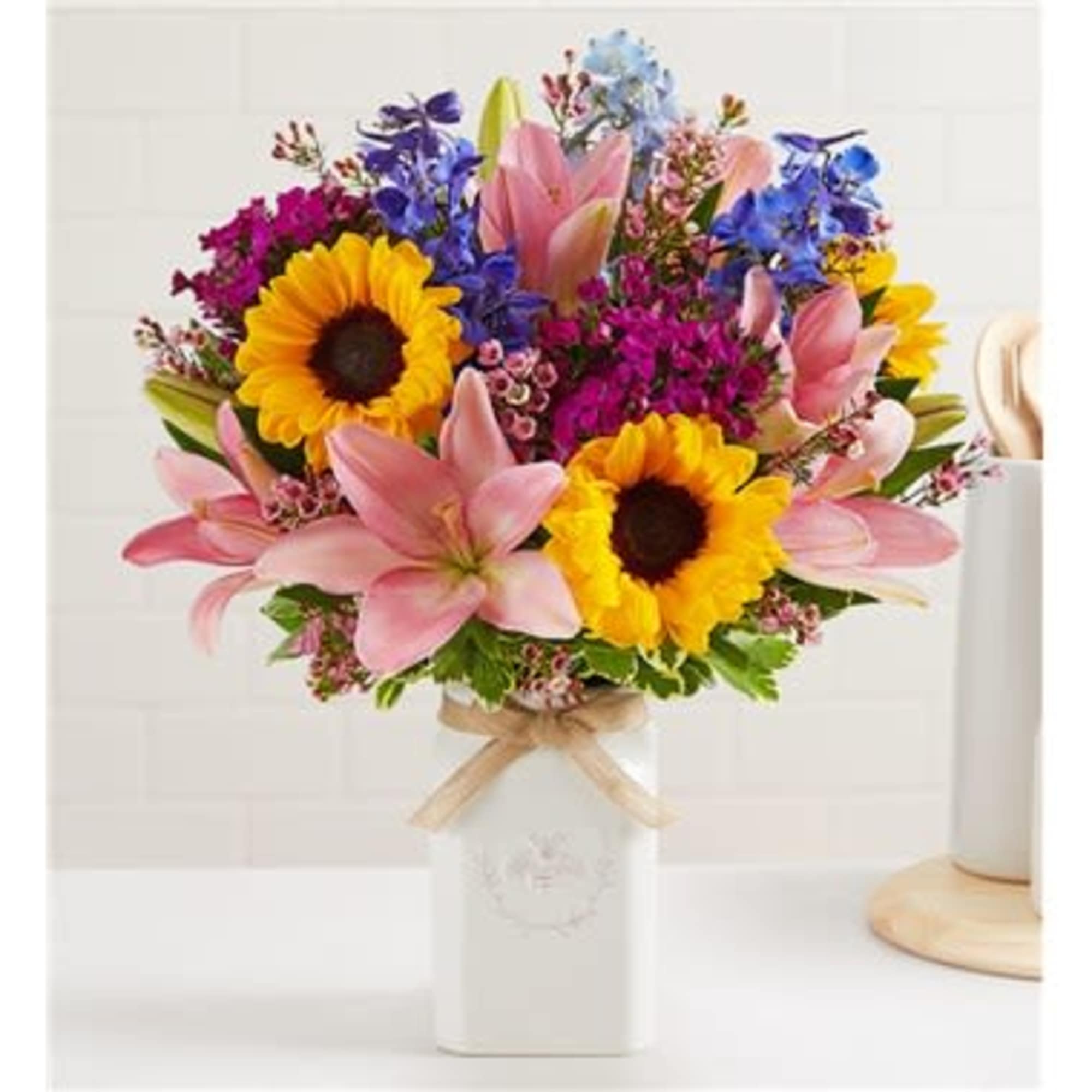 Mixed bouquet with sunflowers, pink lilies, and blue flowers in a white vase
