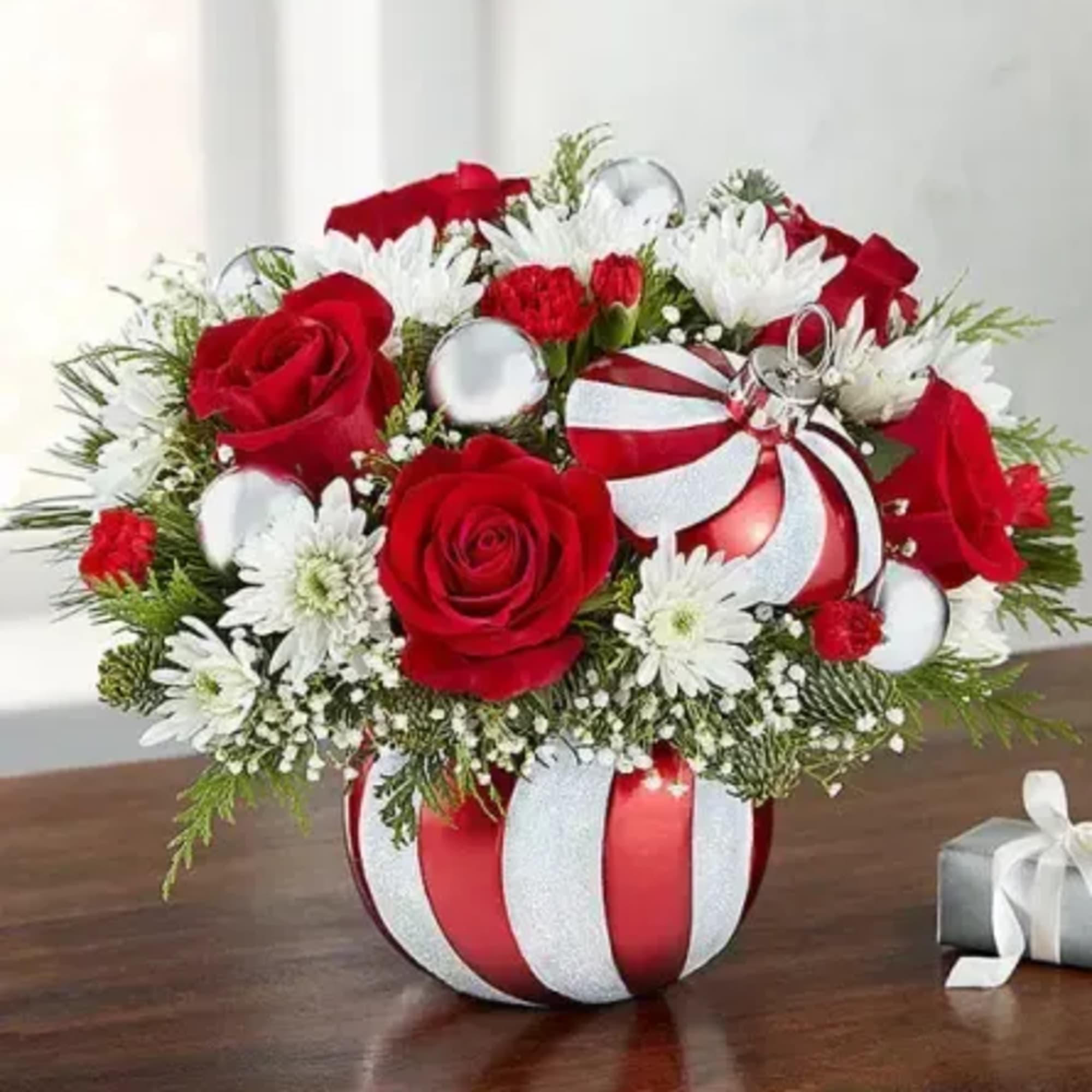 Red roses and white daisies in a striped vase with a gift box