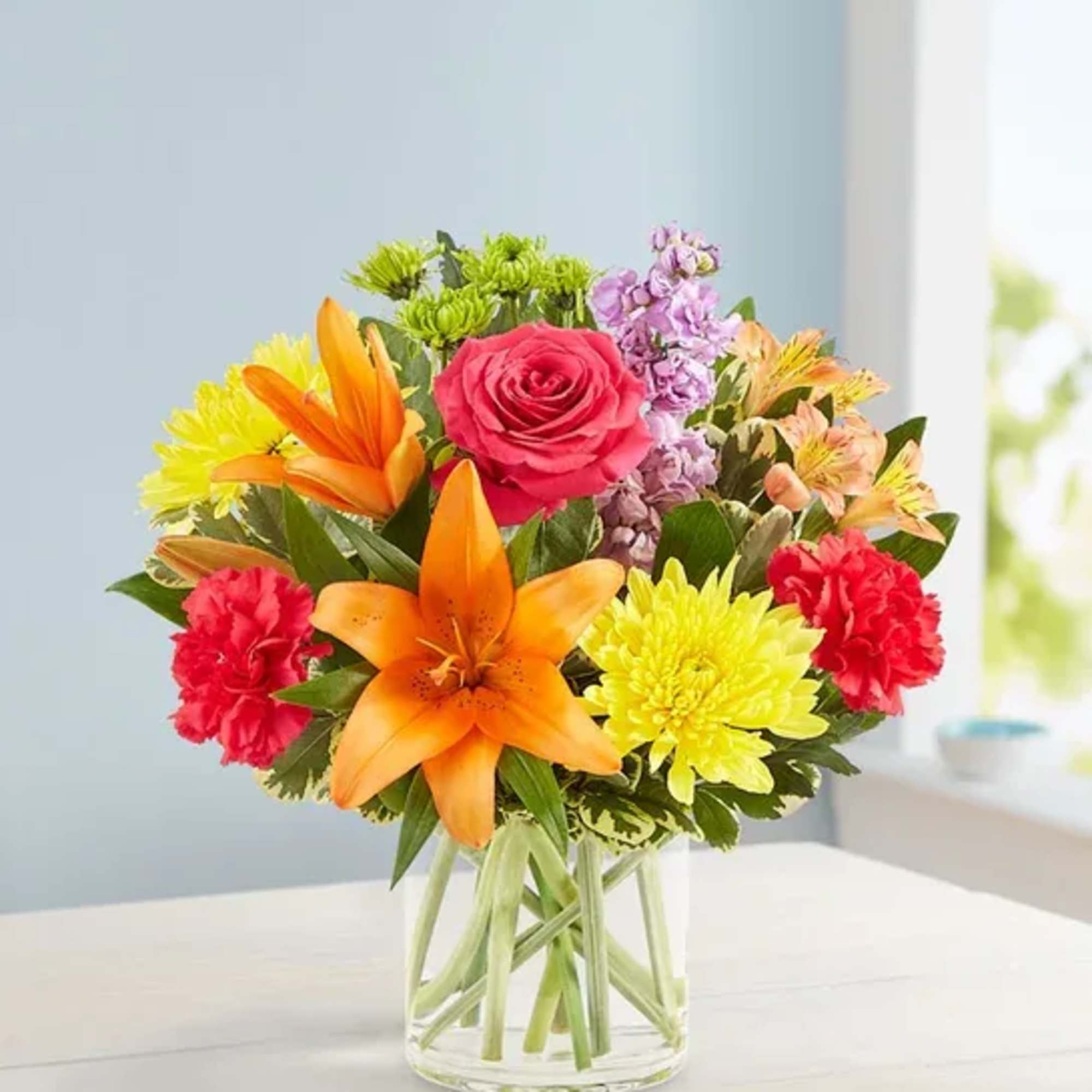 Mixed bouquet with orange lilies, pink rose, and yellow chrysanthemums in a glass vase