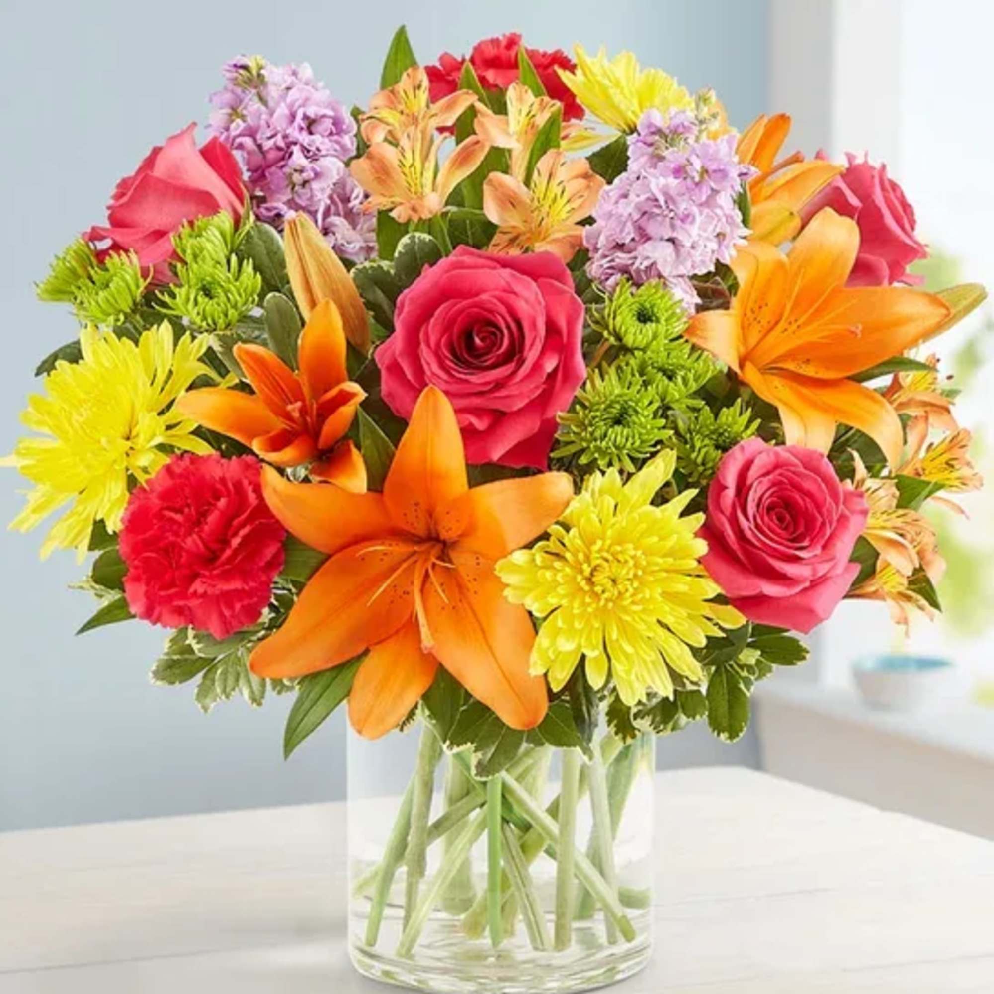 Mixed bouquet of roses, lilies, carnations, and chrysanthemums in a glass vase