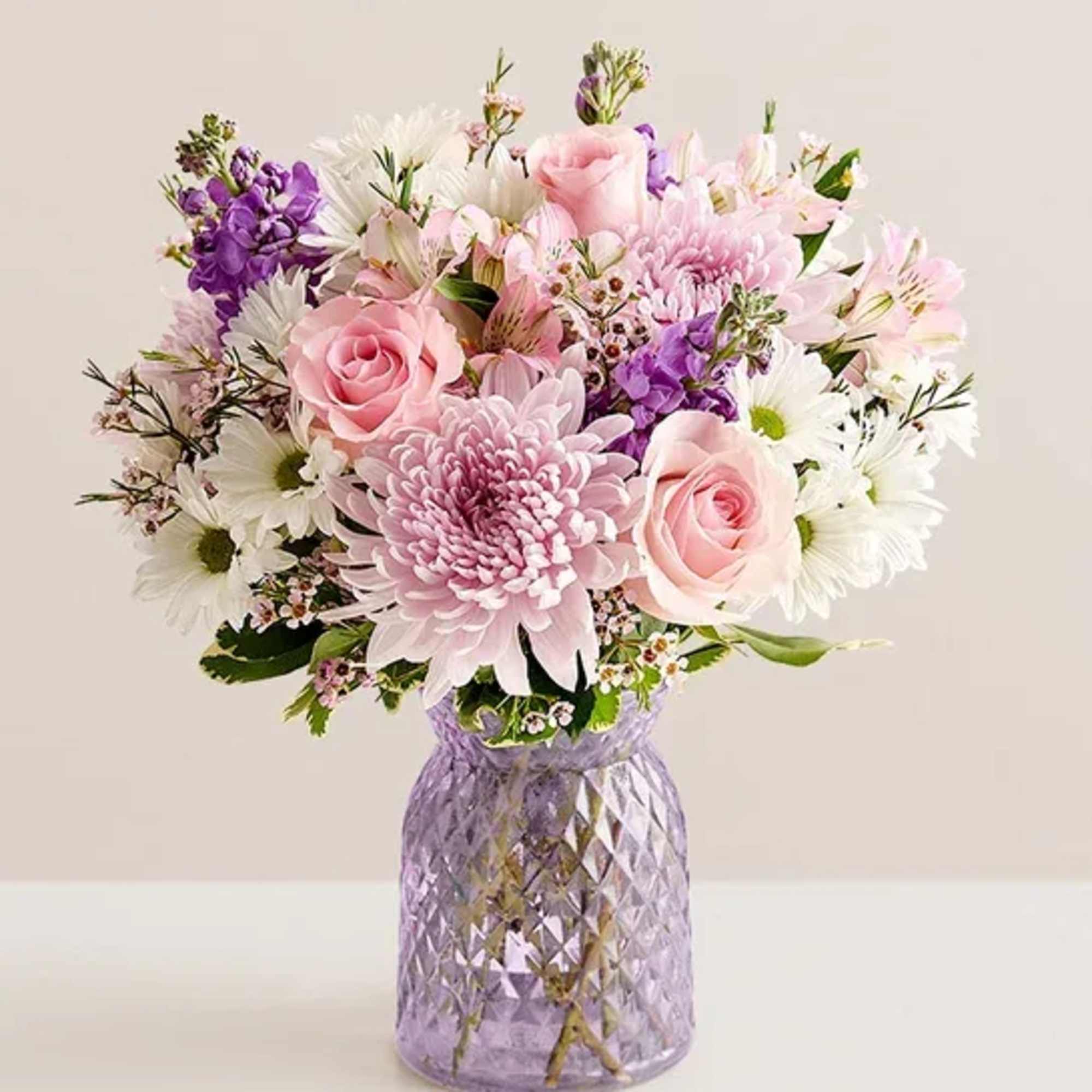 Pastel bouquet of pink roses, white daisies, and mums in a lavender glass vase