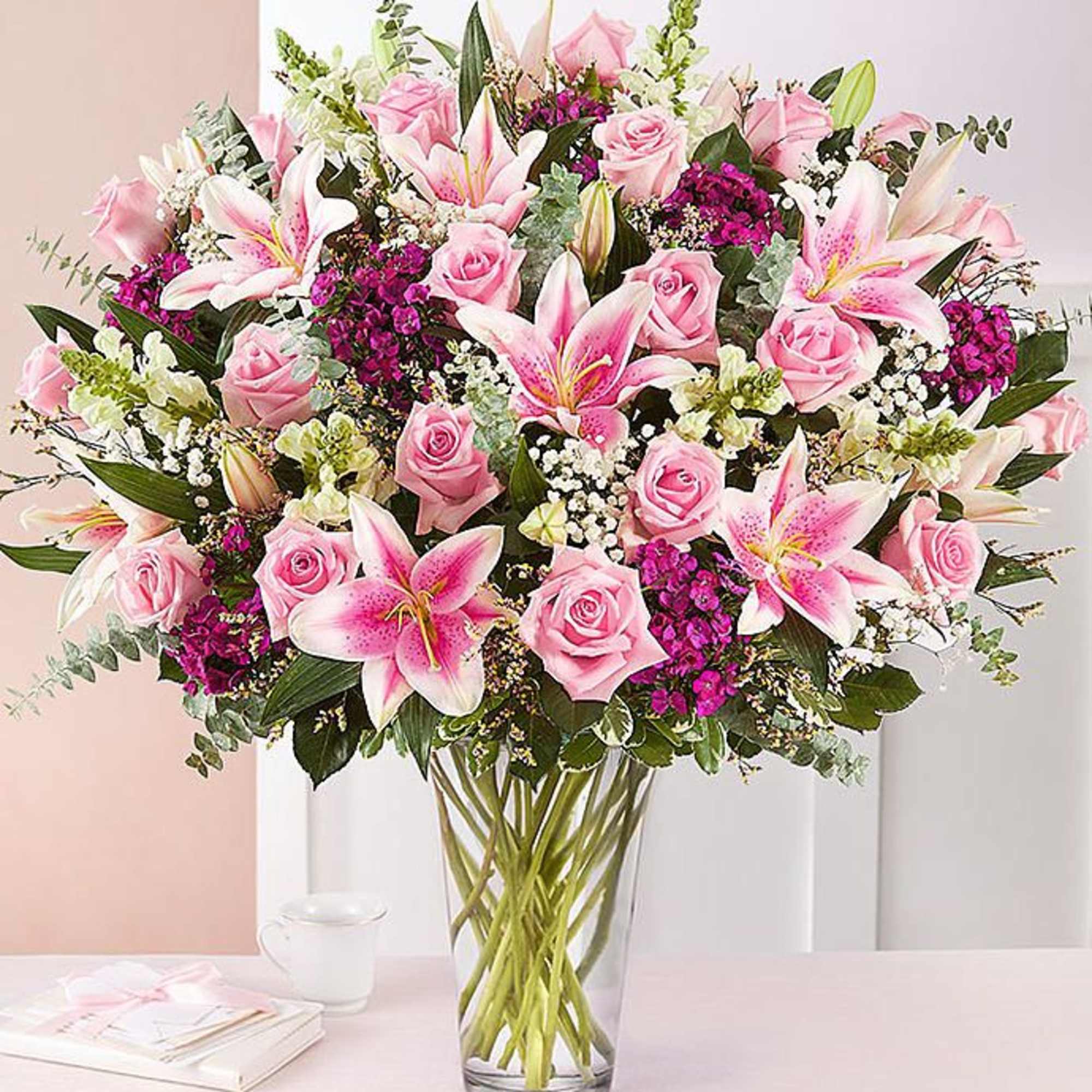 Tall arrangement of pink lilies, pink roses, and white filler flowers in a clear glass vase