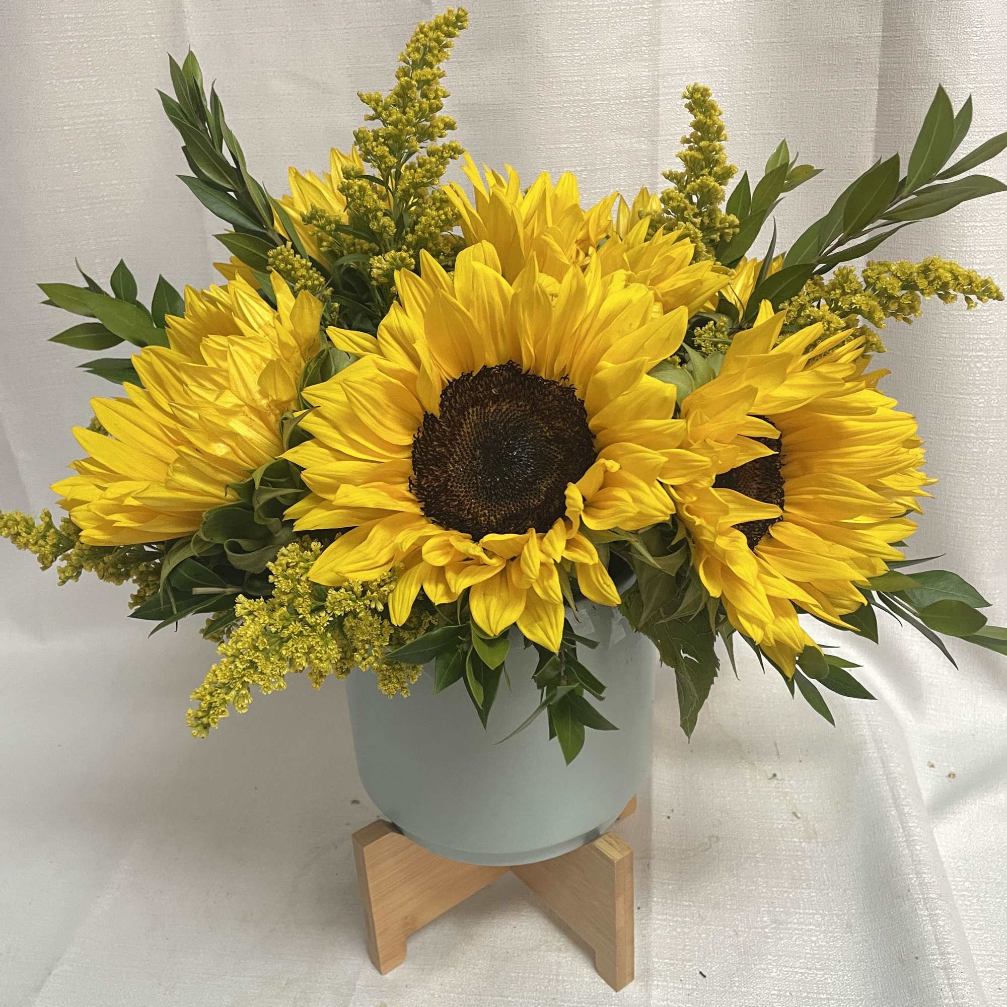 Yellow sunflowers arranged in a pale blue vase with greenery