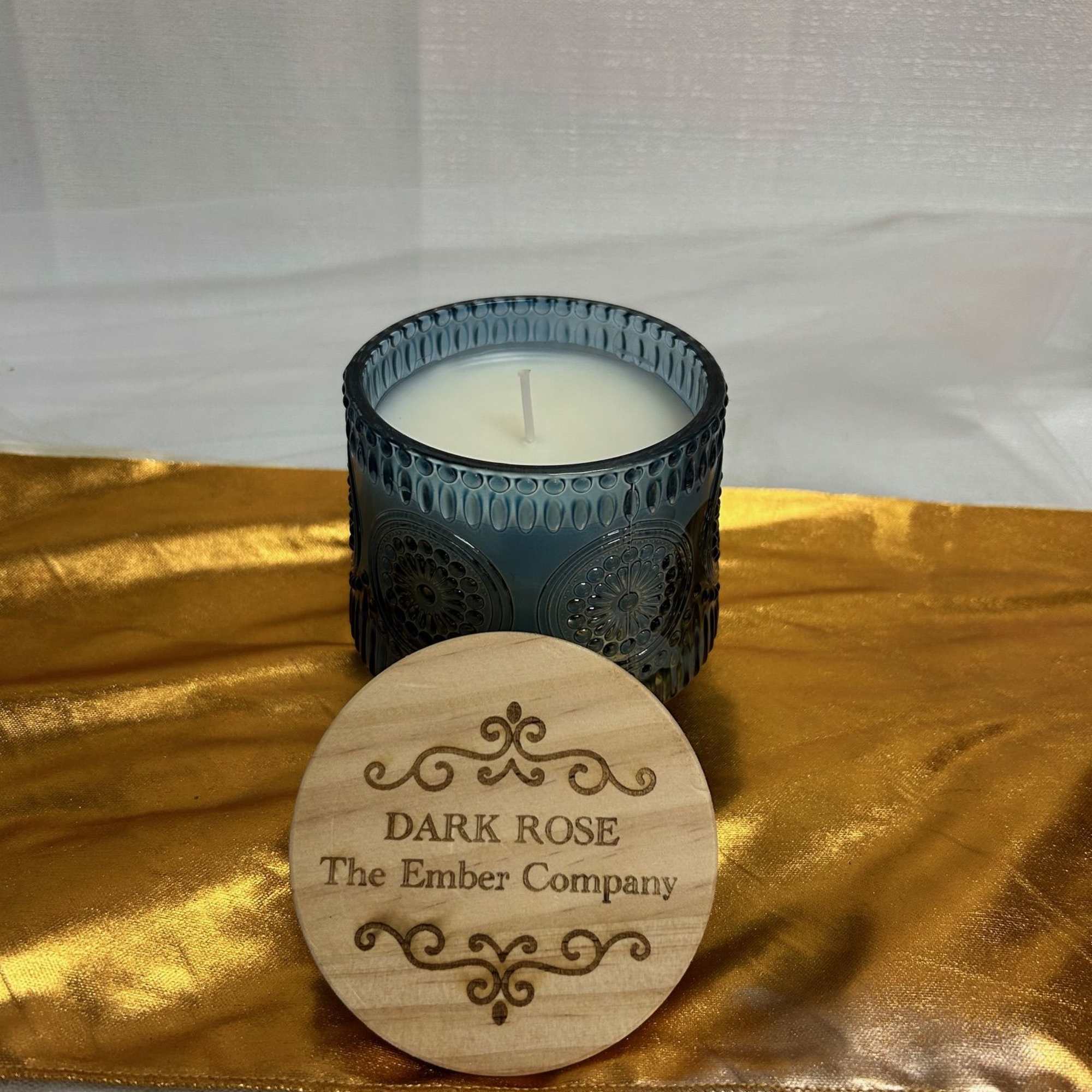 Blue glass candle jar with a wooden lid on gold fabric