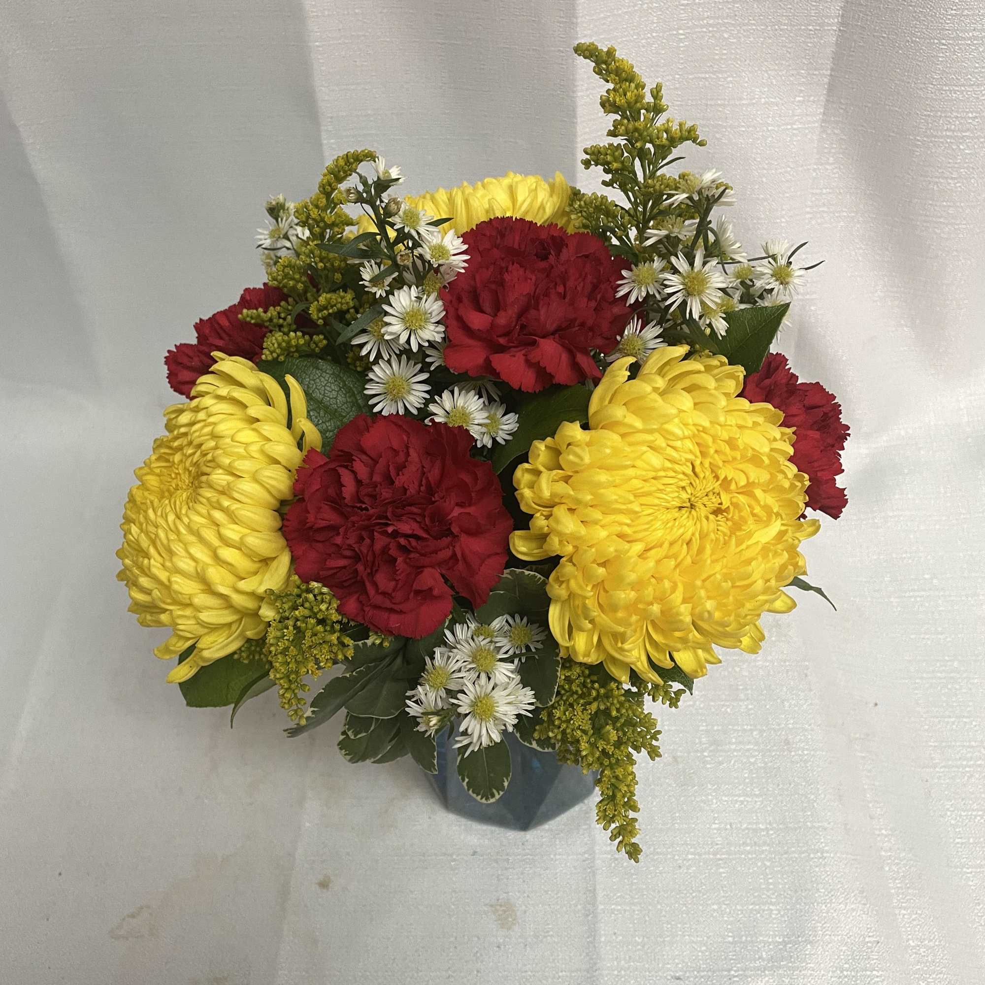 Bouquet of yellow chrysanthemums, red carnations, and small white daisies in a vase