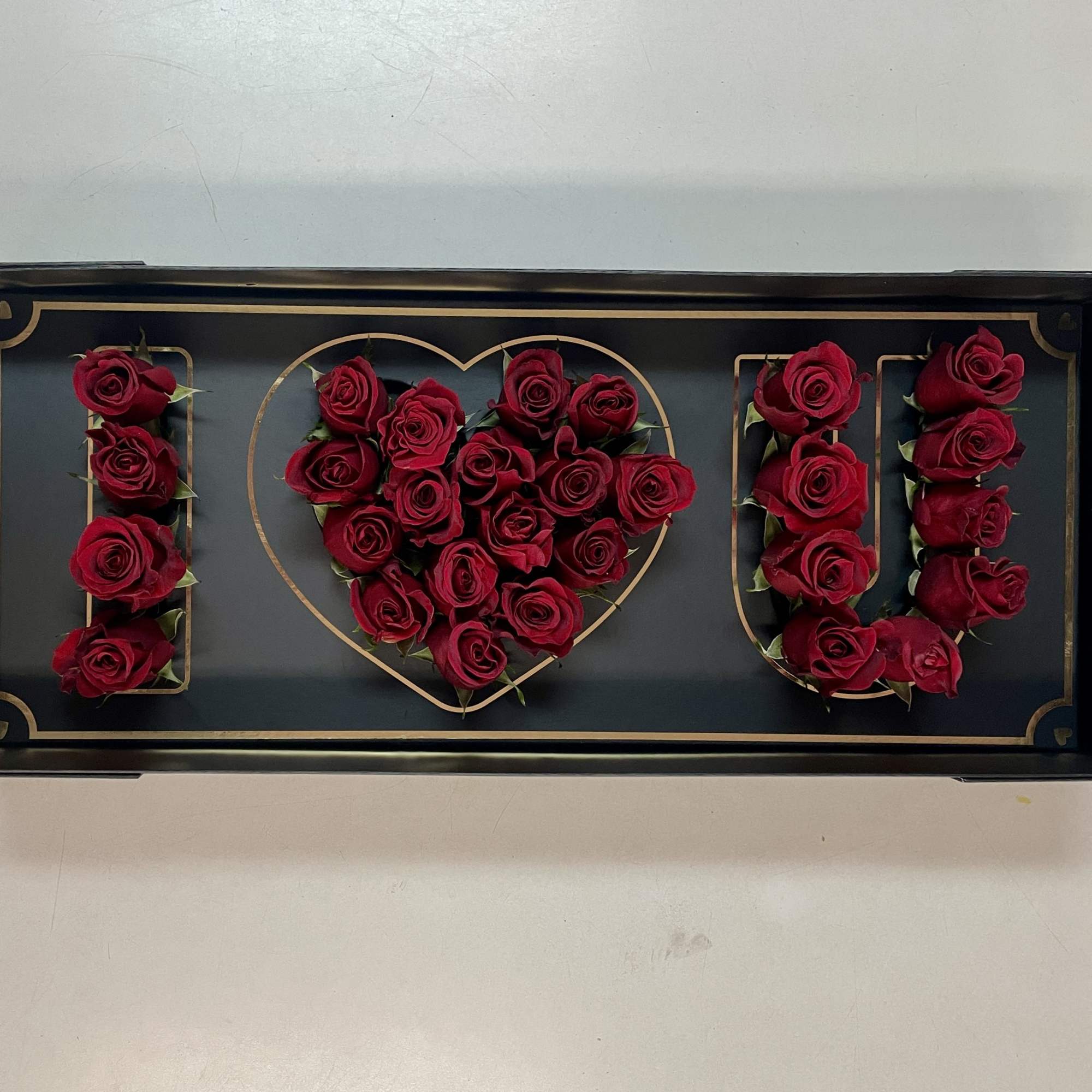Red roses arranged to spell "I ♥ U" in a black tray