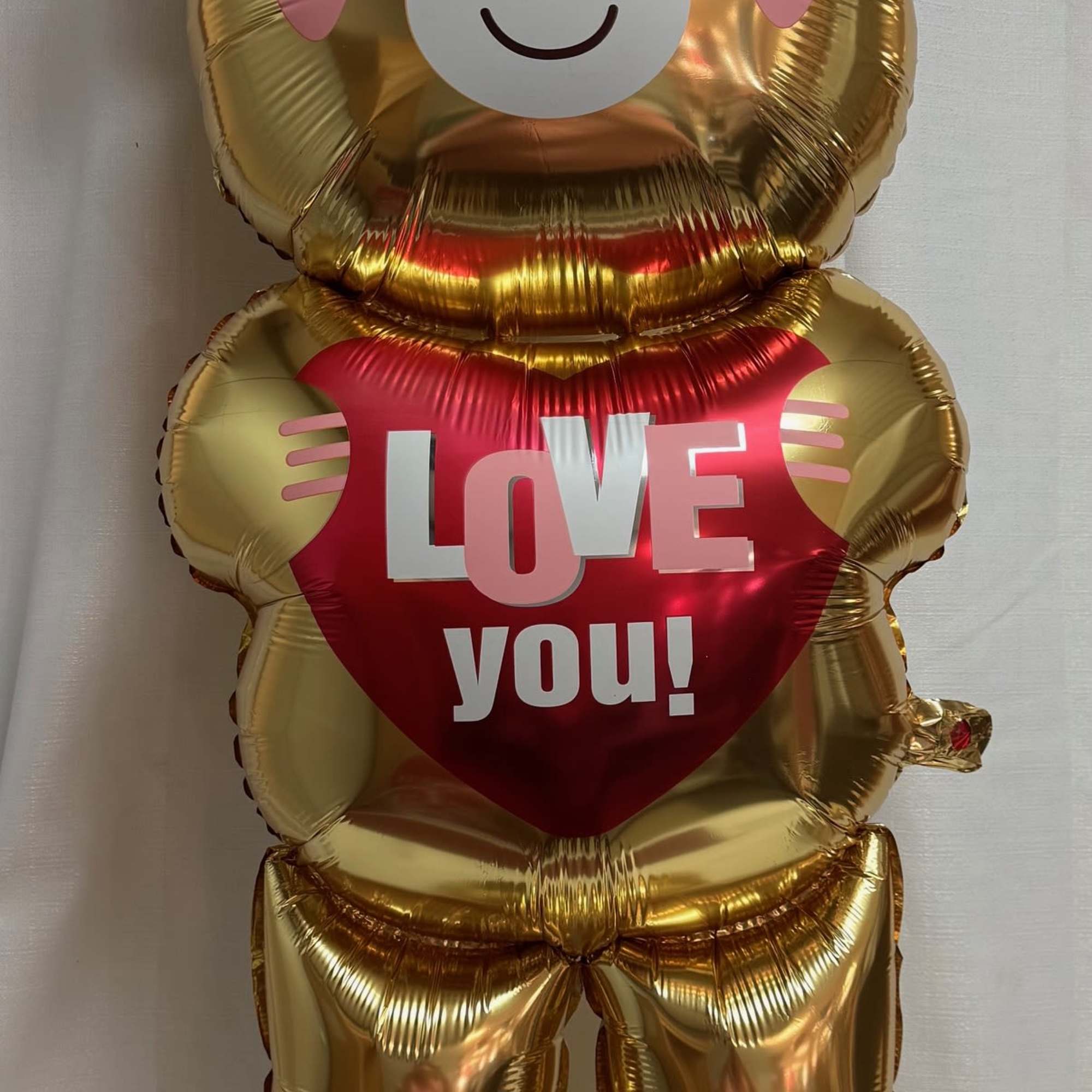 Gold teddy bear balloon holding a red heart that says "LOVE you!"