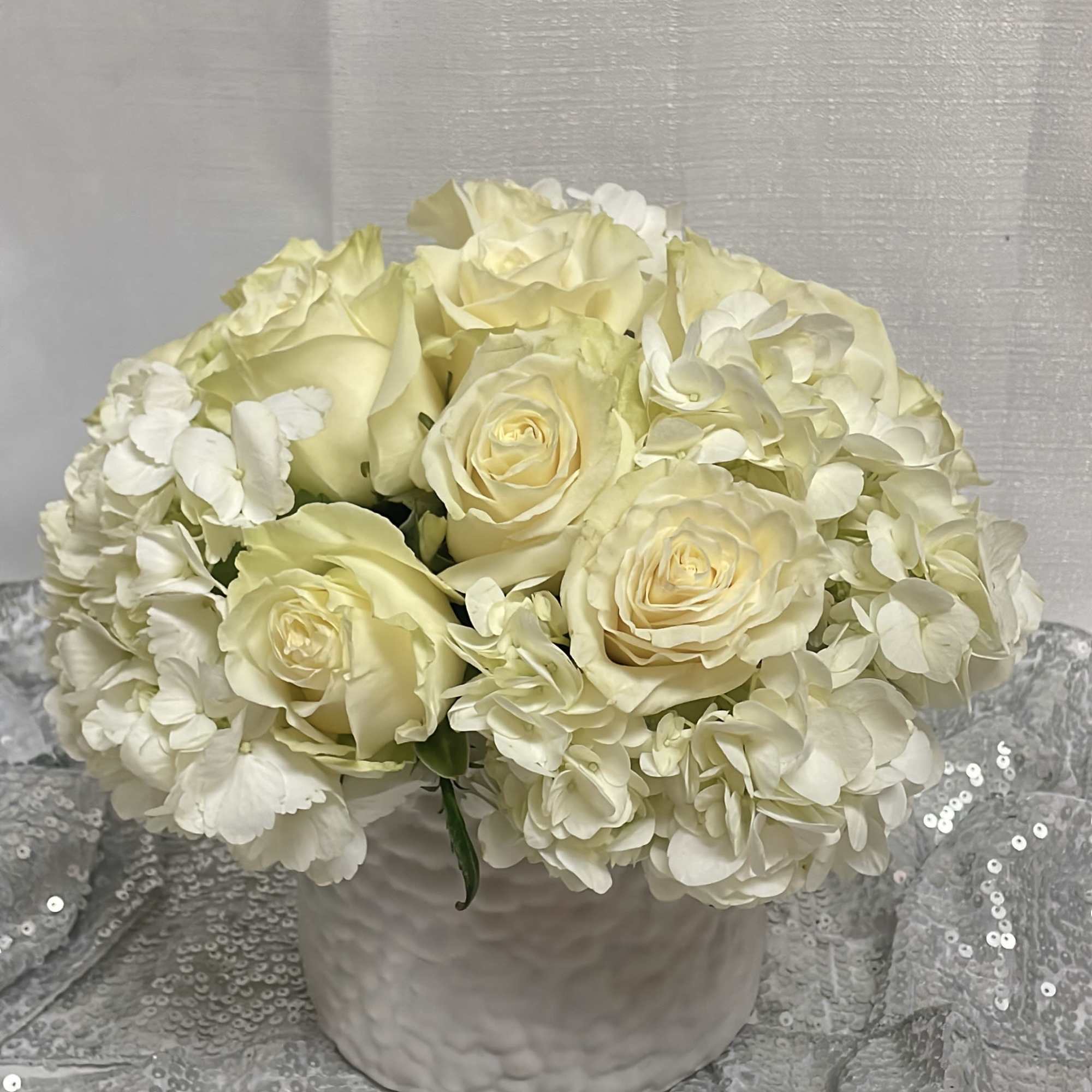 Cream roses and white hydrangeas arranged in a white vase