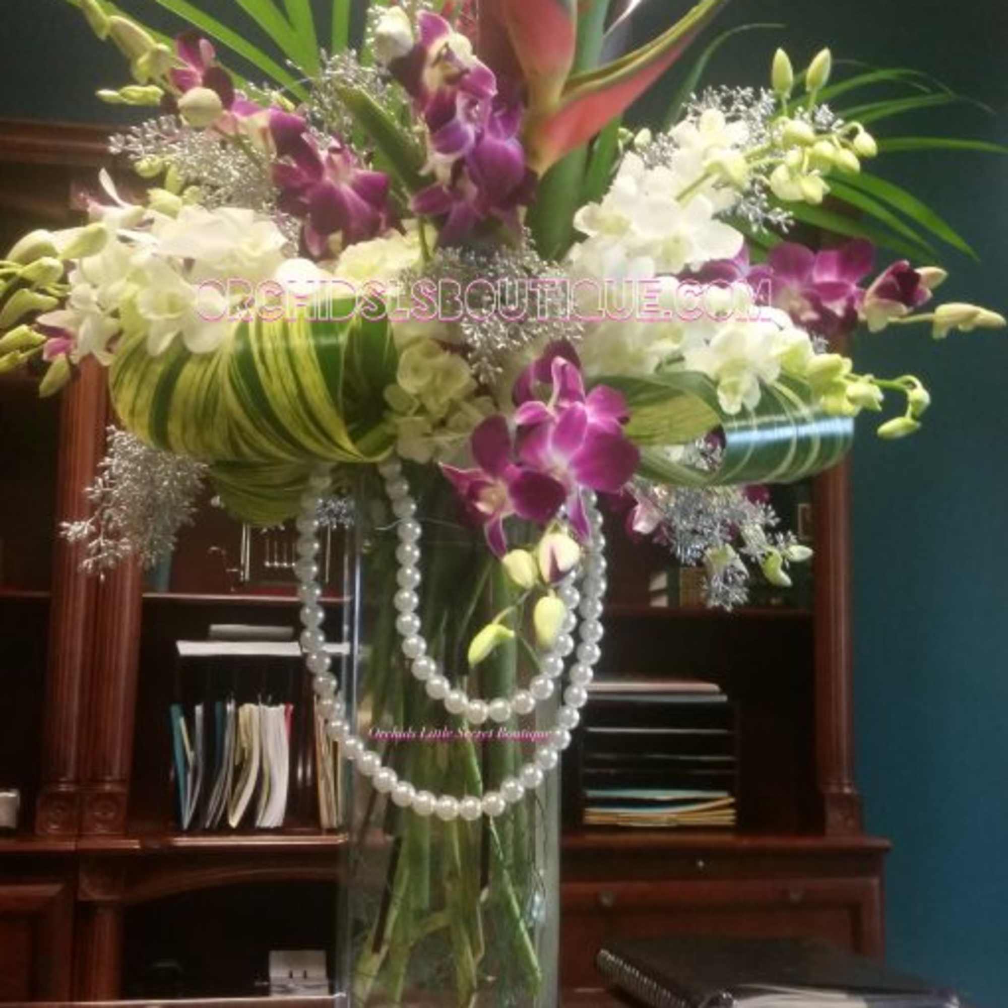 Tall orchid arrangement in a clear glass vase with pearl strands
