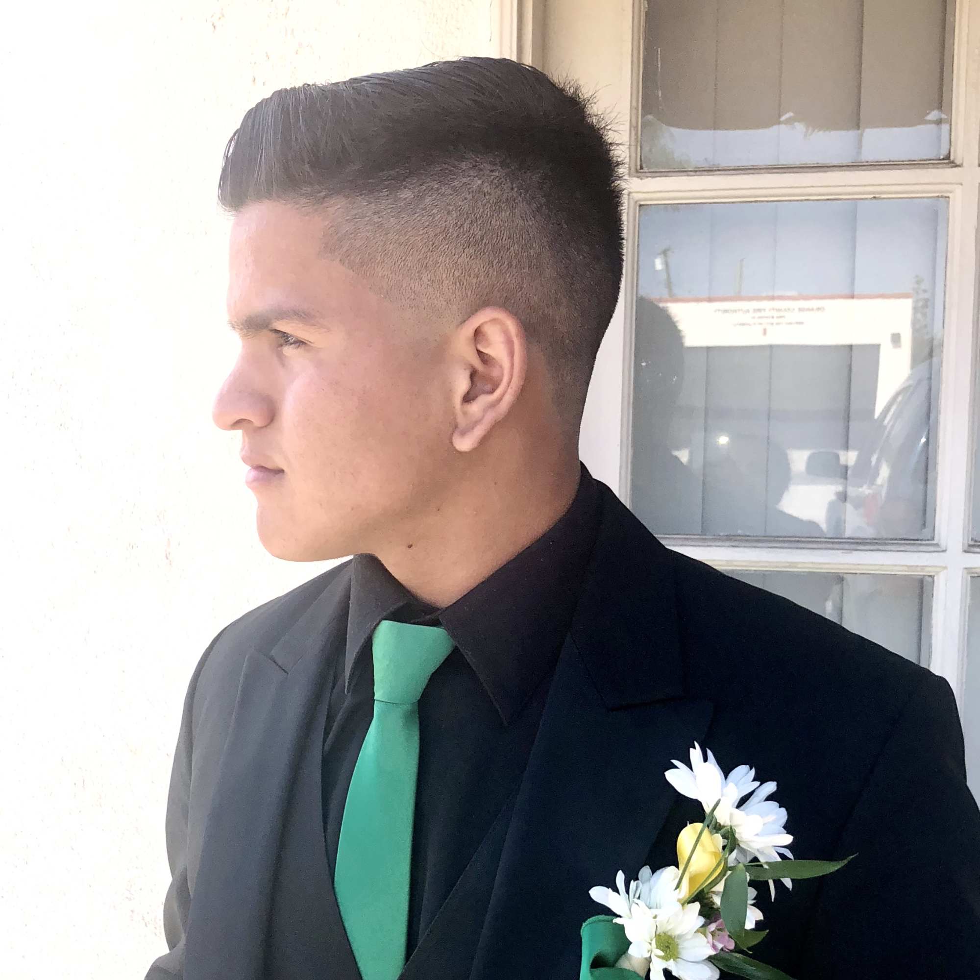 Man in a black suit with a white boutonniere and green tie