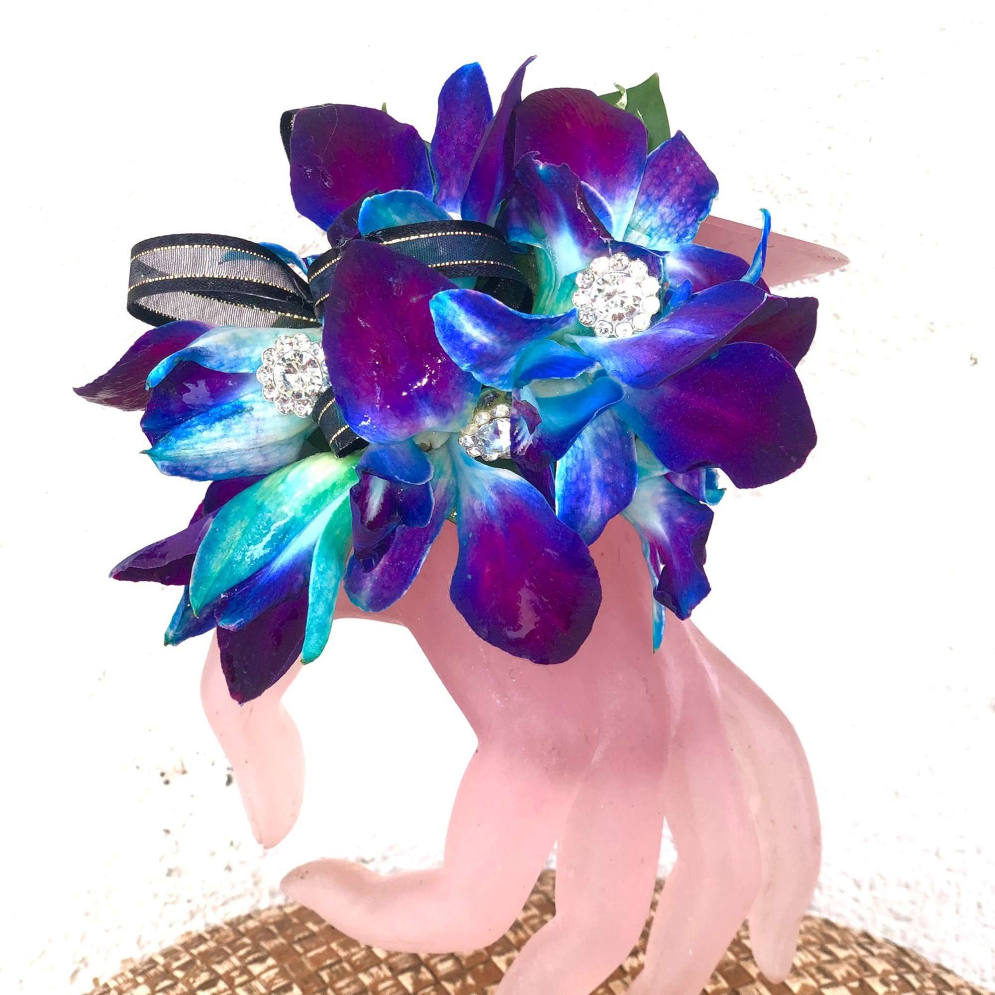 Blue and purple orchid bouquet with ribbon on a pink hand sculpture
