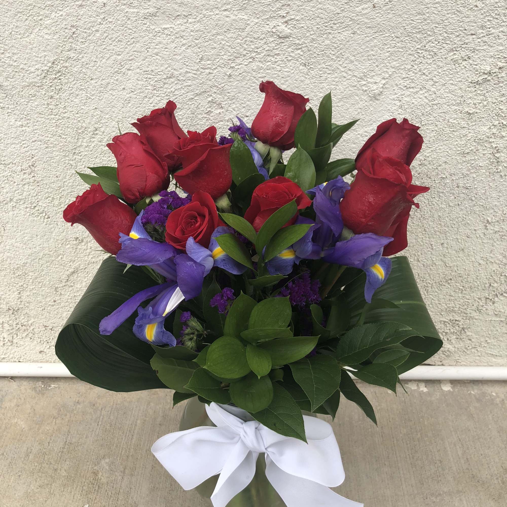 Bouquet of red roses and purple irises in a glass vase with a white ribbon