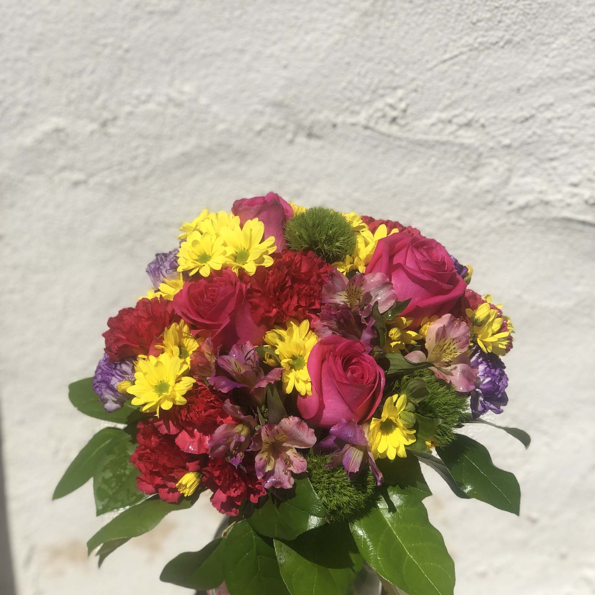 Bouquet of pink roses, yellow daisies, and red carnations in a glass vase