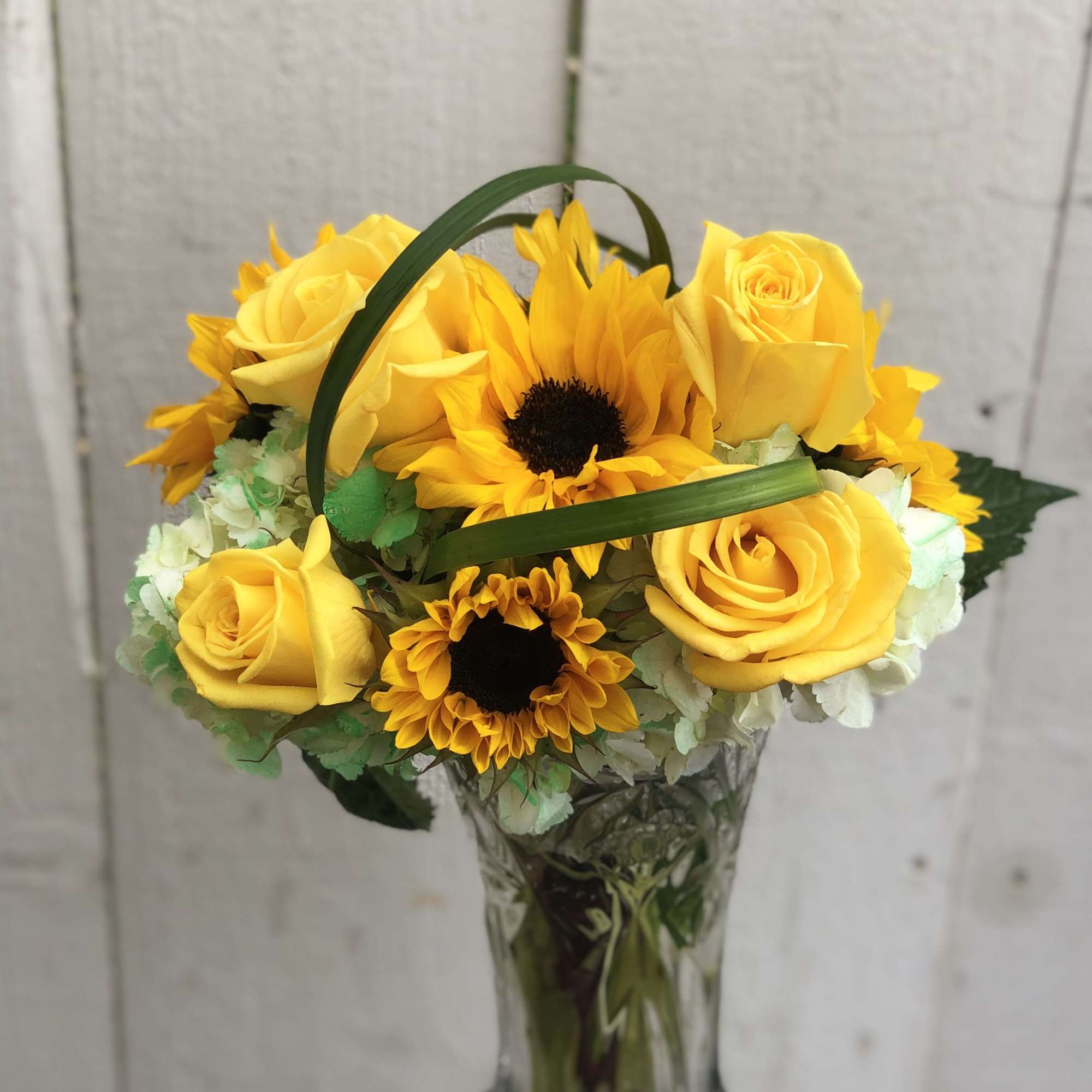 Yellow roses and sunflowers arranged in a clear glass vase
