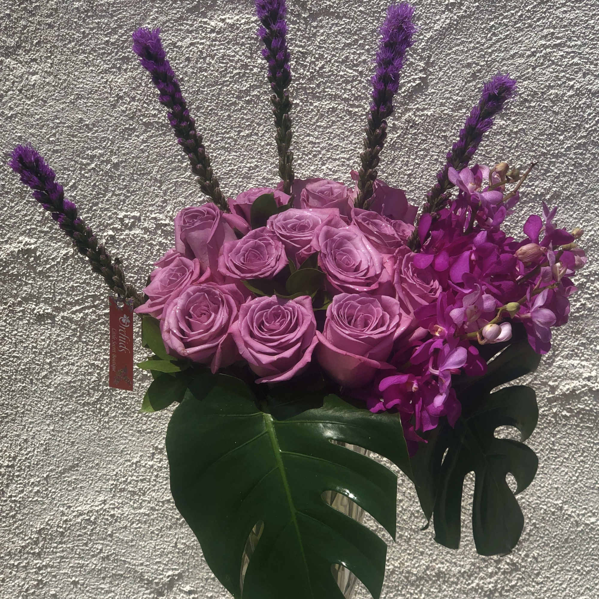 Pink roses and purple orchids in a glass vase with large tropical leaves