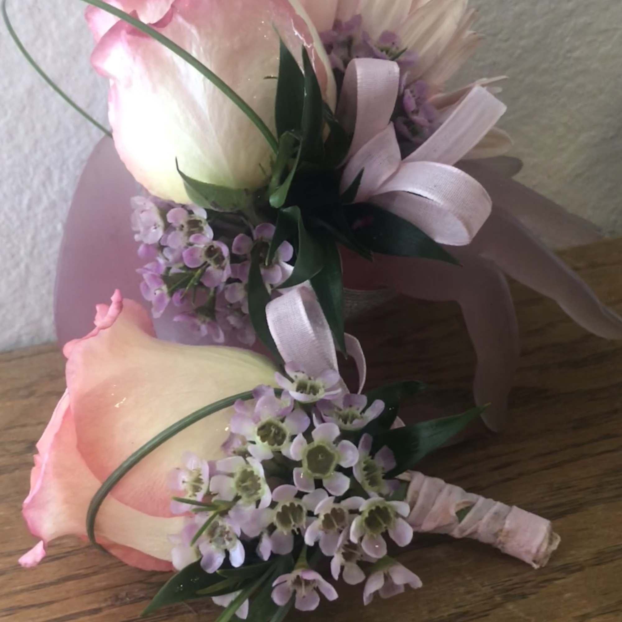 Two pink-and-white floral boutonnieres with ribbon accents