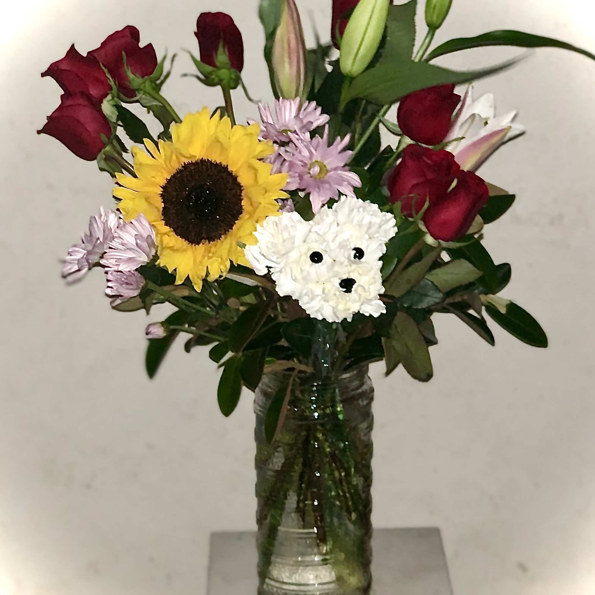 Bouquet of red roses, a sunflower, and a white teddy bear in a glass vase