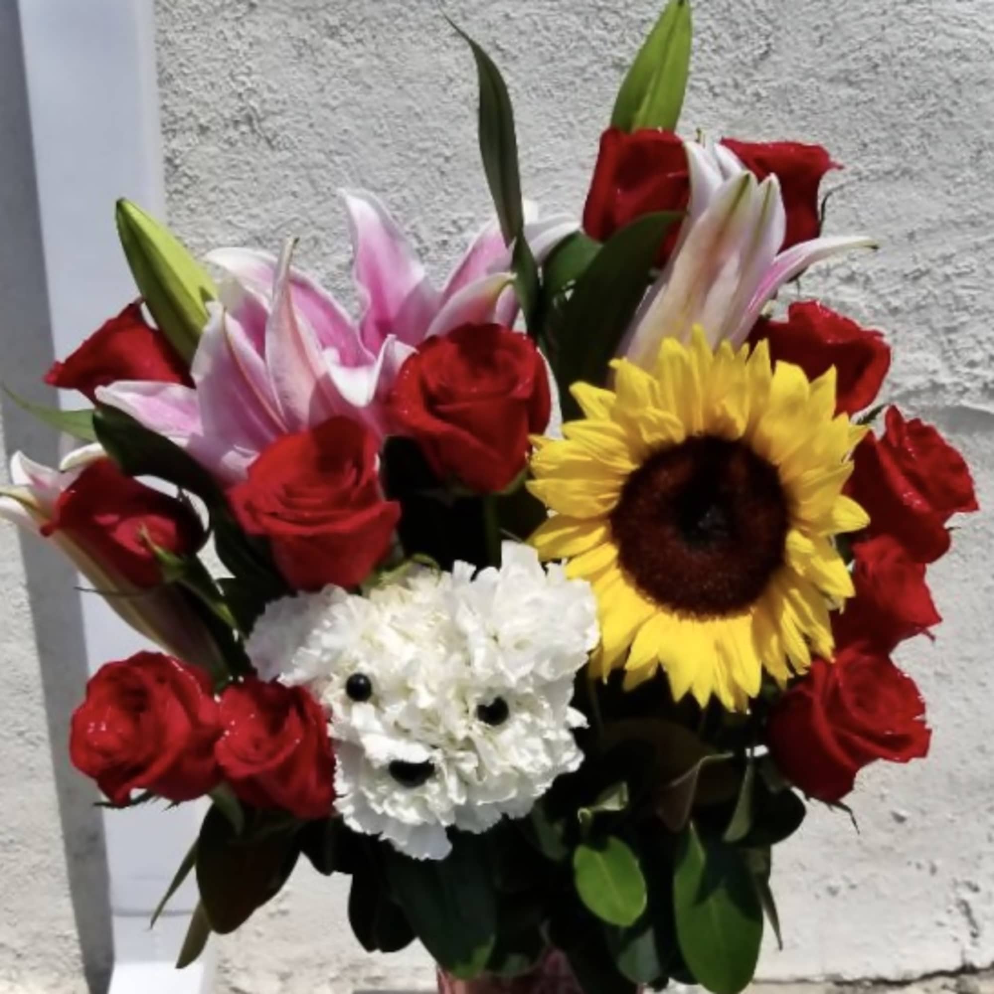 Bouquet of red roses, pink lilies, and a sunflower in a vase