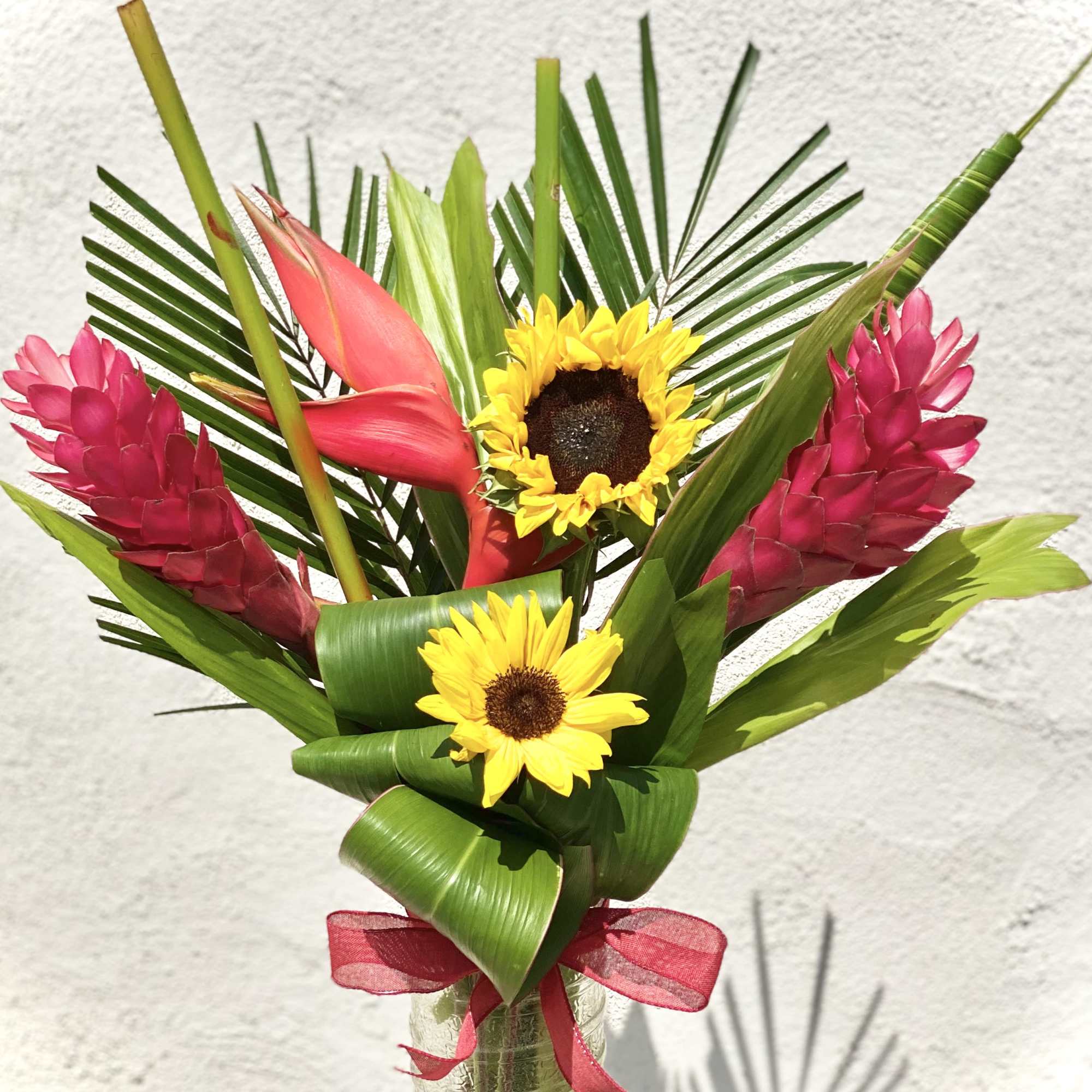 Tropical bouquet with sunflowers and pink ginger in a glass vase
