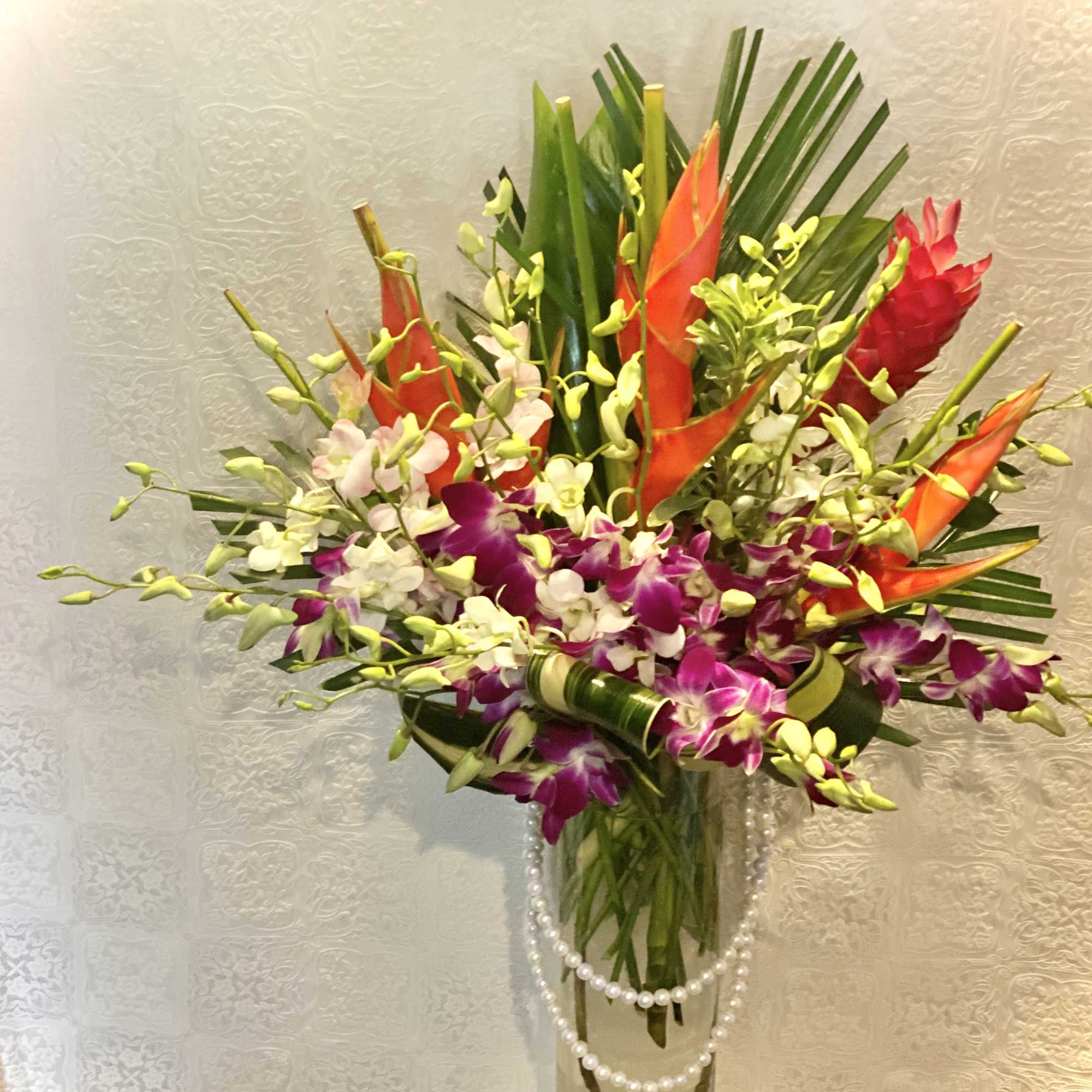 Tropical bouquet with orchids and orange heliconia in a glass vase
