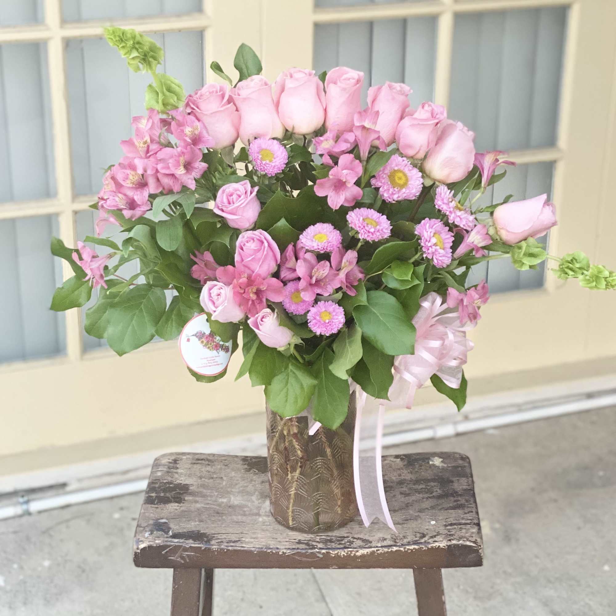 Pink roses and mixed pink flowers in a tall vase with a ribbon