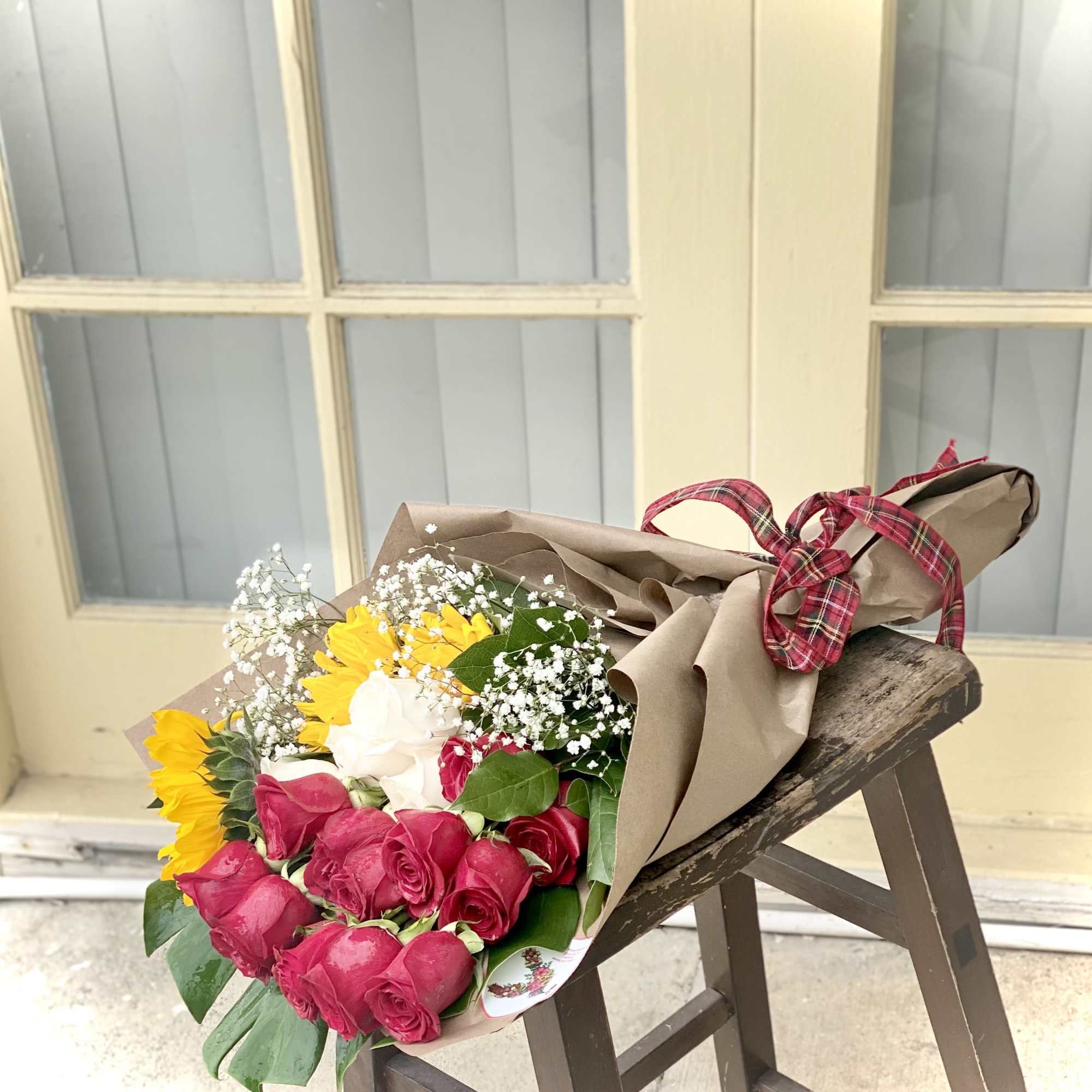 Bouquet of pink roses, yellow sunflowers, and white baby's breath in brown paper