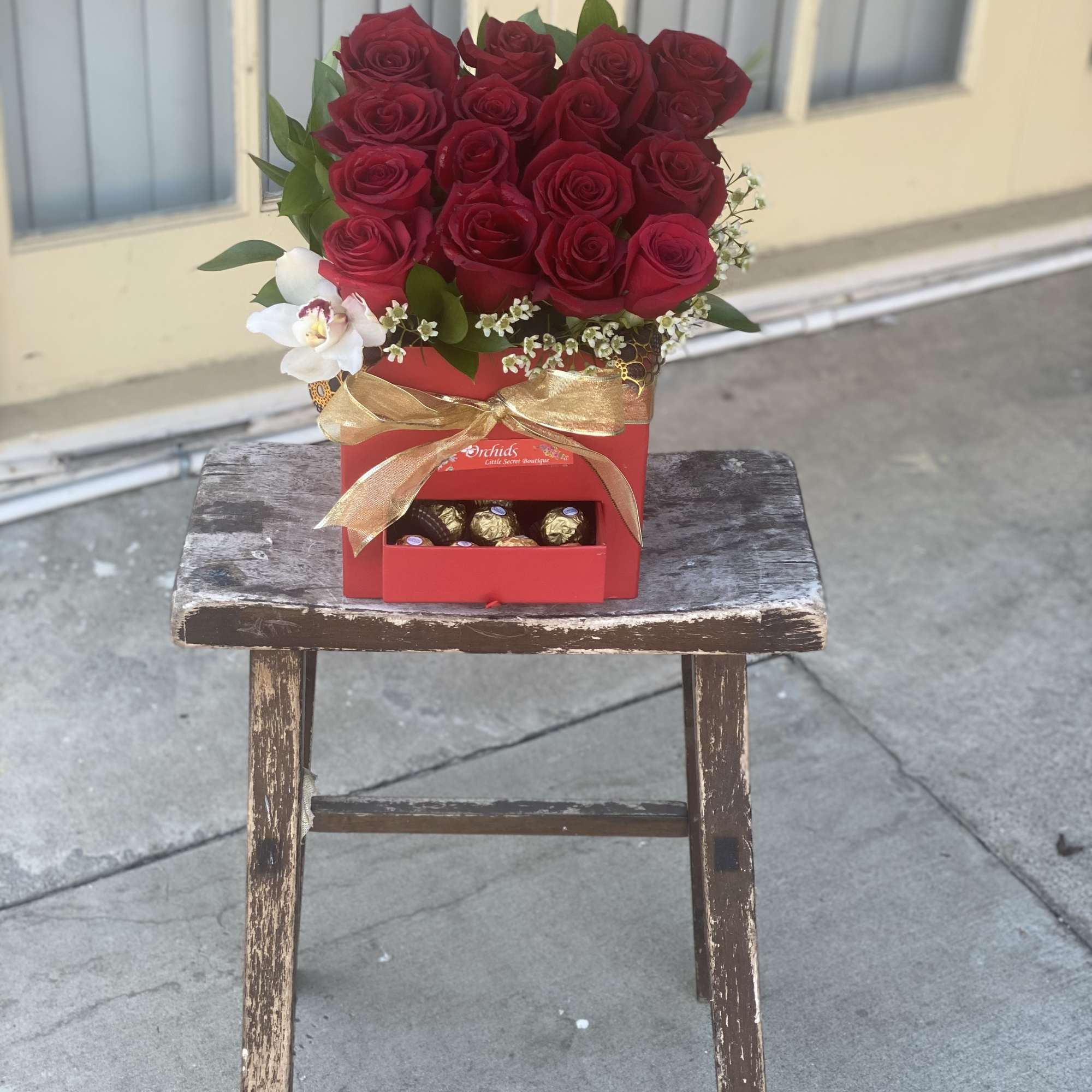 Red rose arrangement in a red gift box with chocolates and a gold ribbon