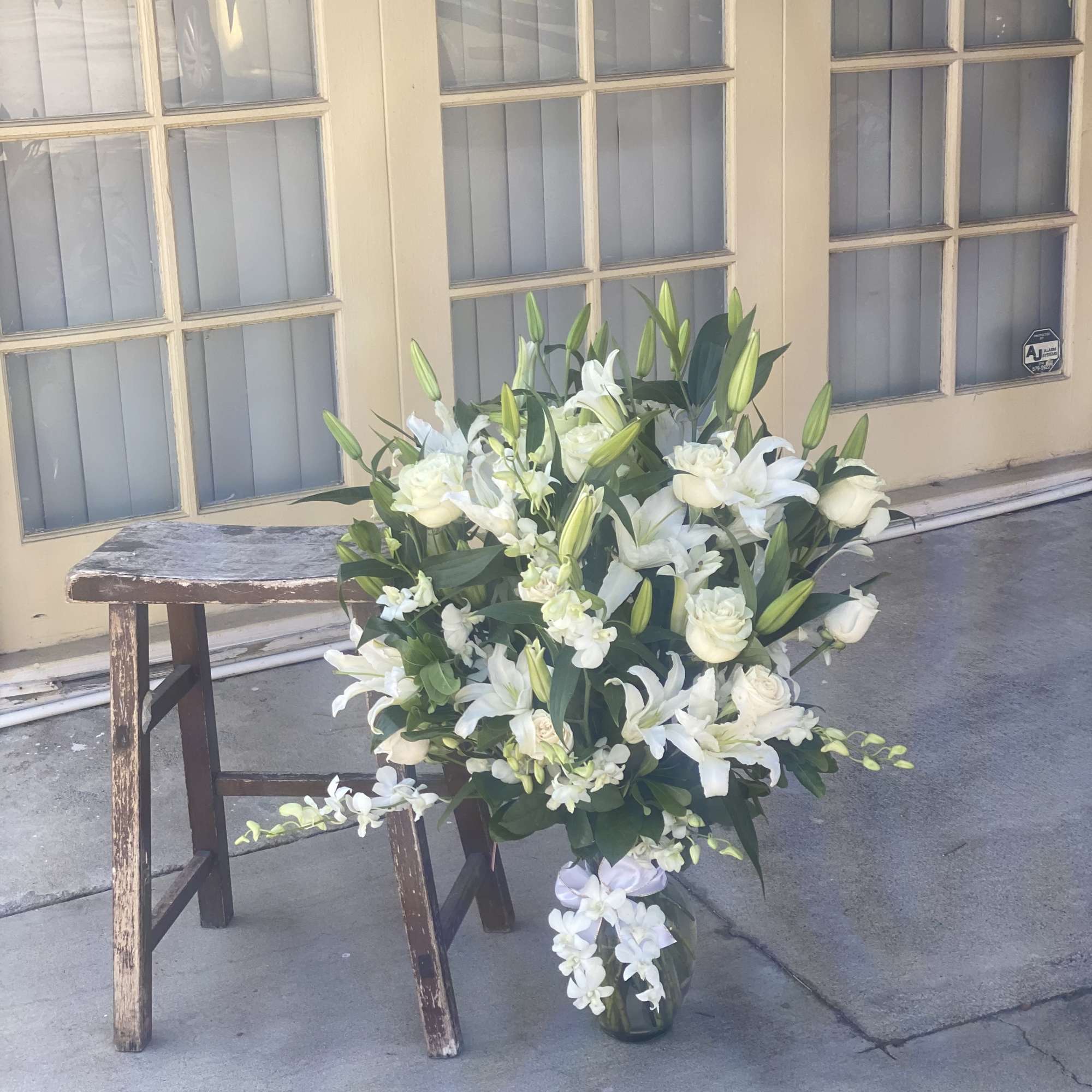 White lilies and roses arranged in a glass vase on the ground