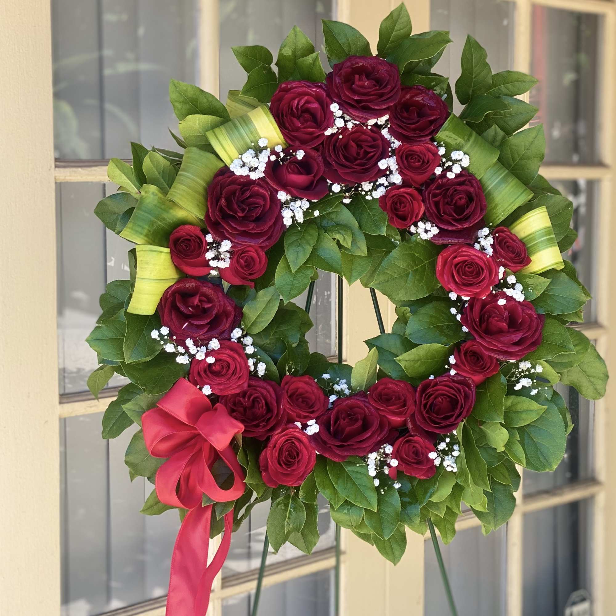 Circular wreath of red roses with white baby's breath and a pink ribbon