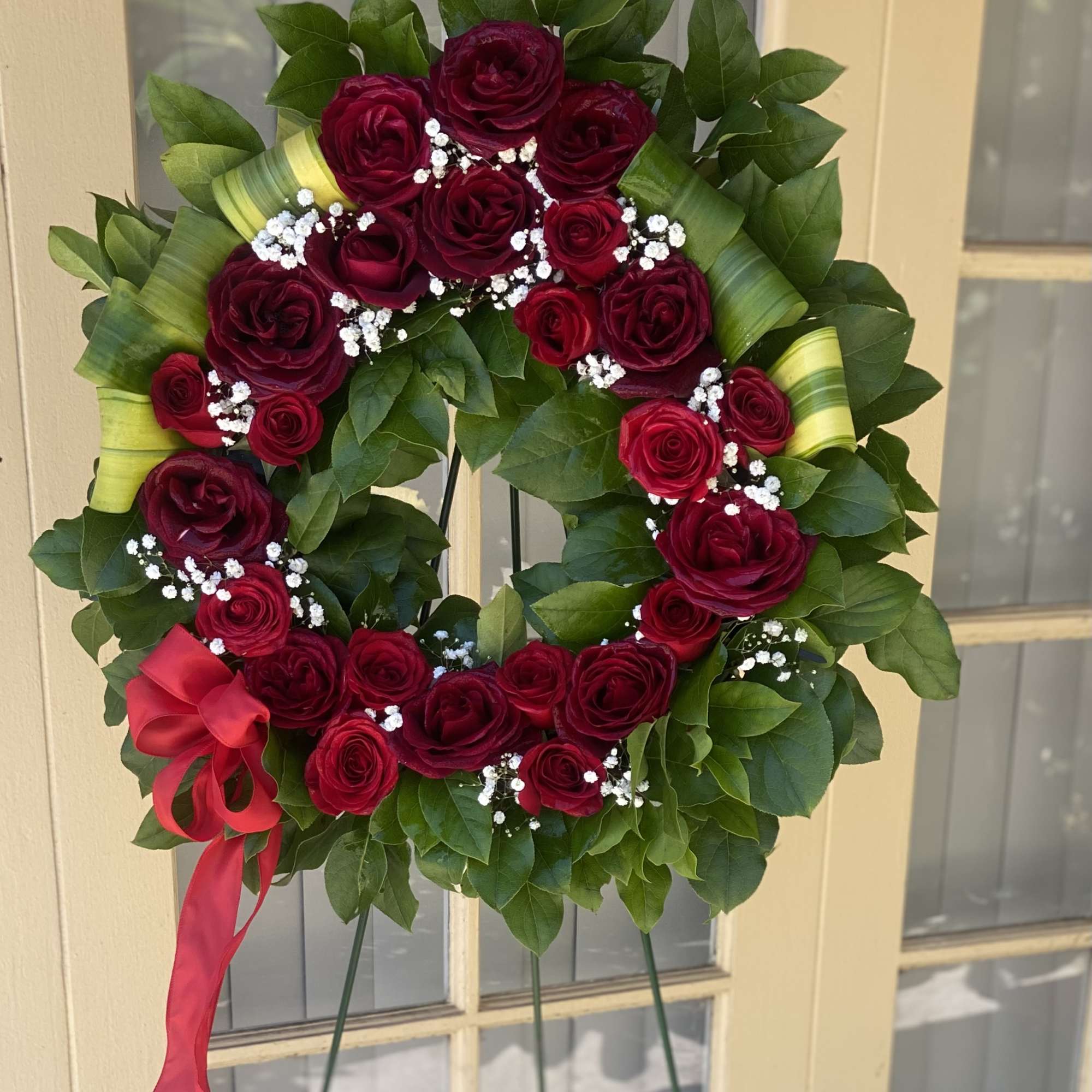 Heart-shaped wreath of red roses with a red ribbon on a stand