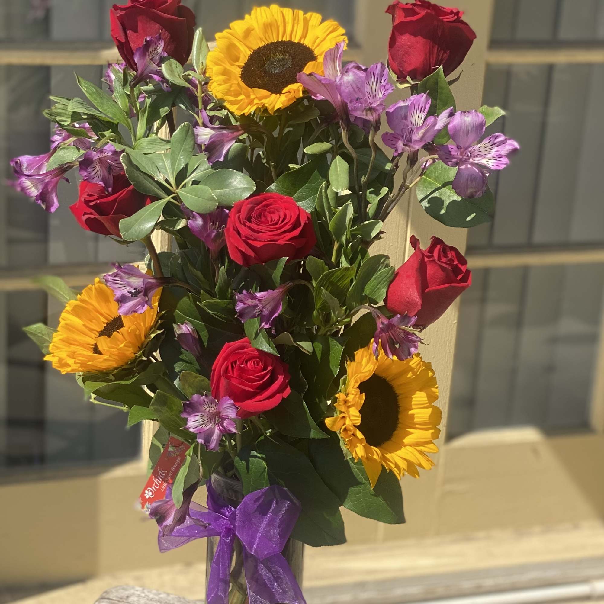 Bouquet of red roses, sunflowers, and purple flowers in a glass vase