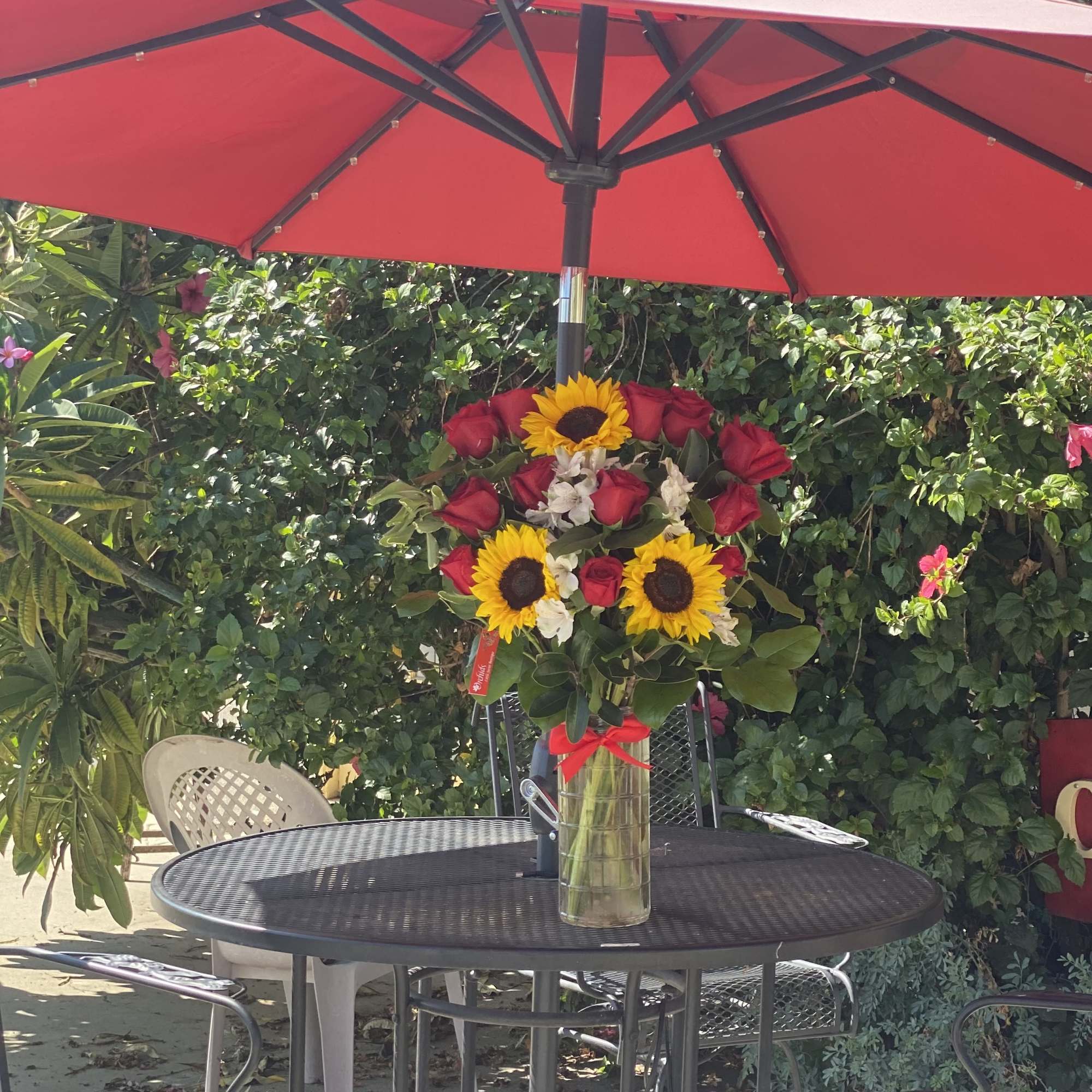 Red roses and sunflowers arranged in a clear vase on a patio table