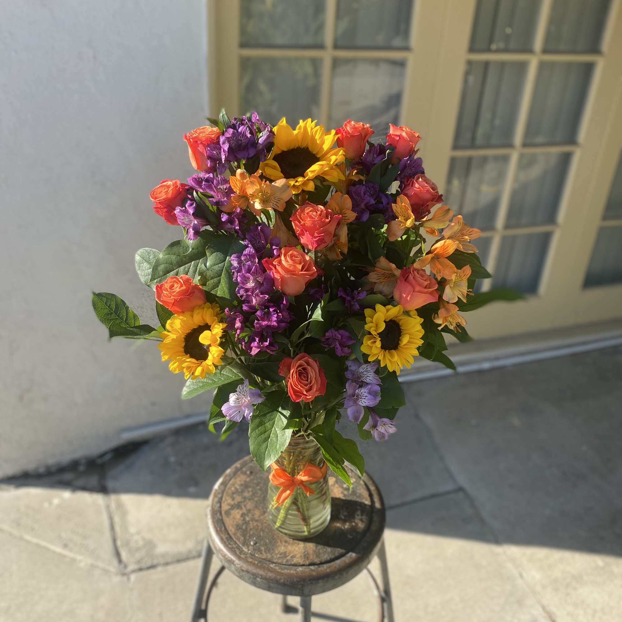 Mixed bouquet with sunflowers, roses, and purple flowers in a glass vase