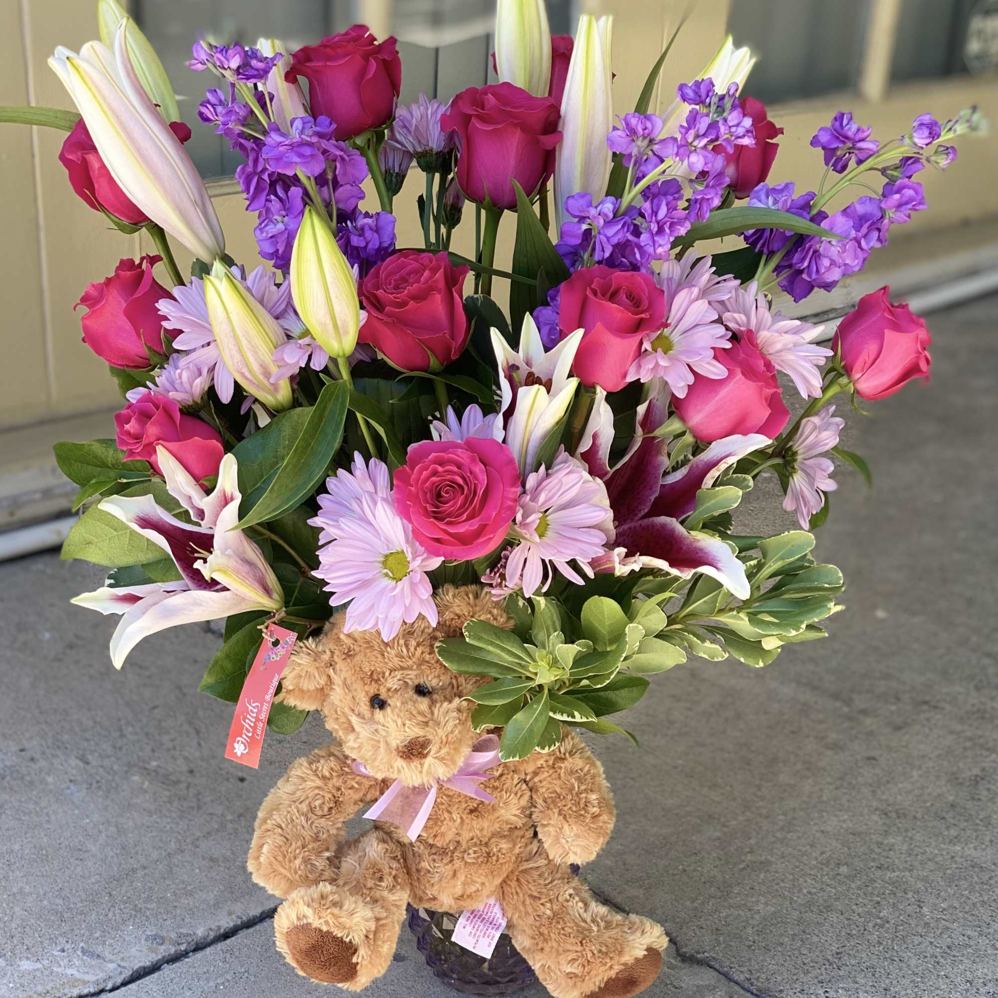 Bouquet of pink roses, lilies, and purple flowers with a teddy bear base