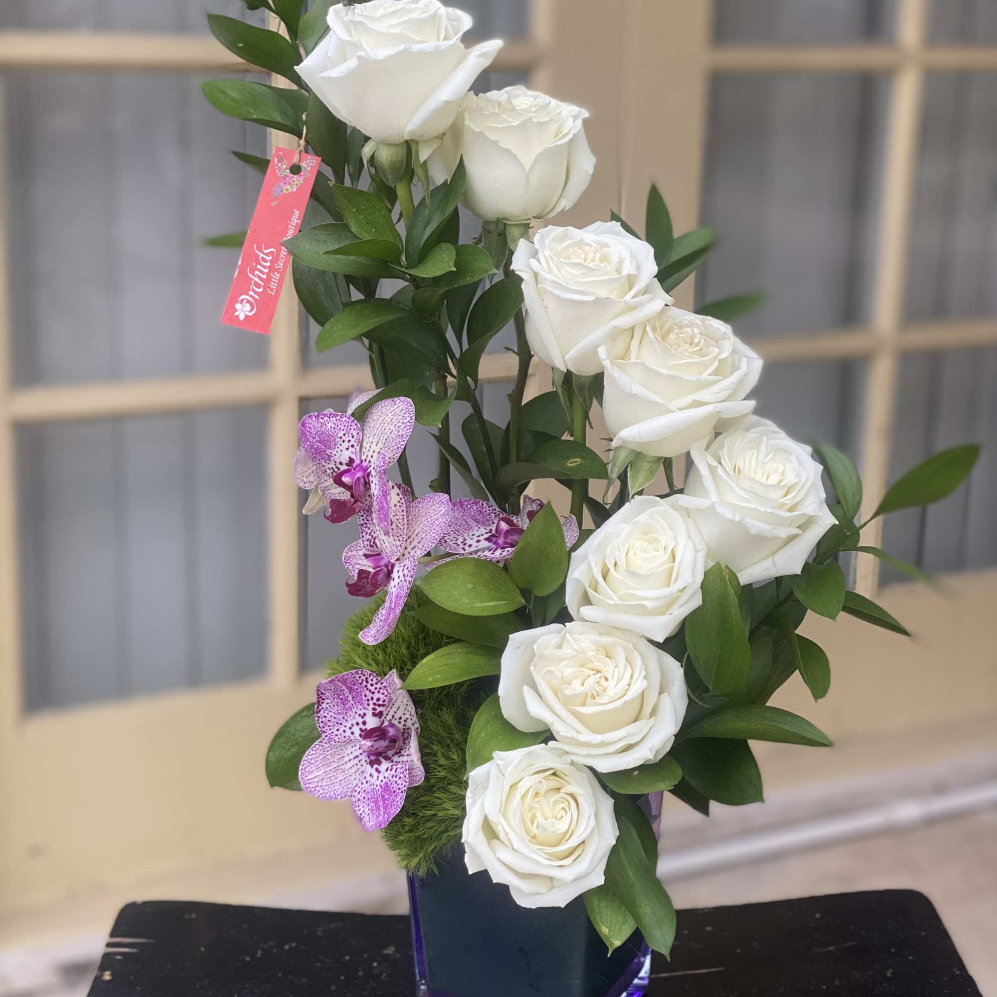 White roses and purple orchids arranged in a glass vase