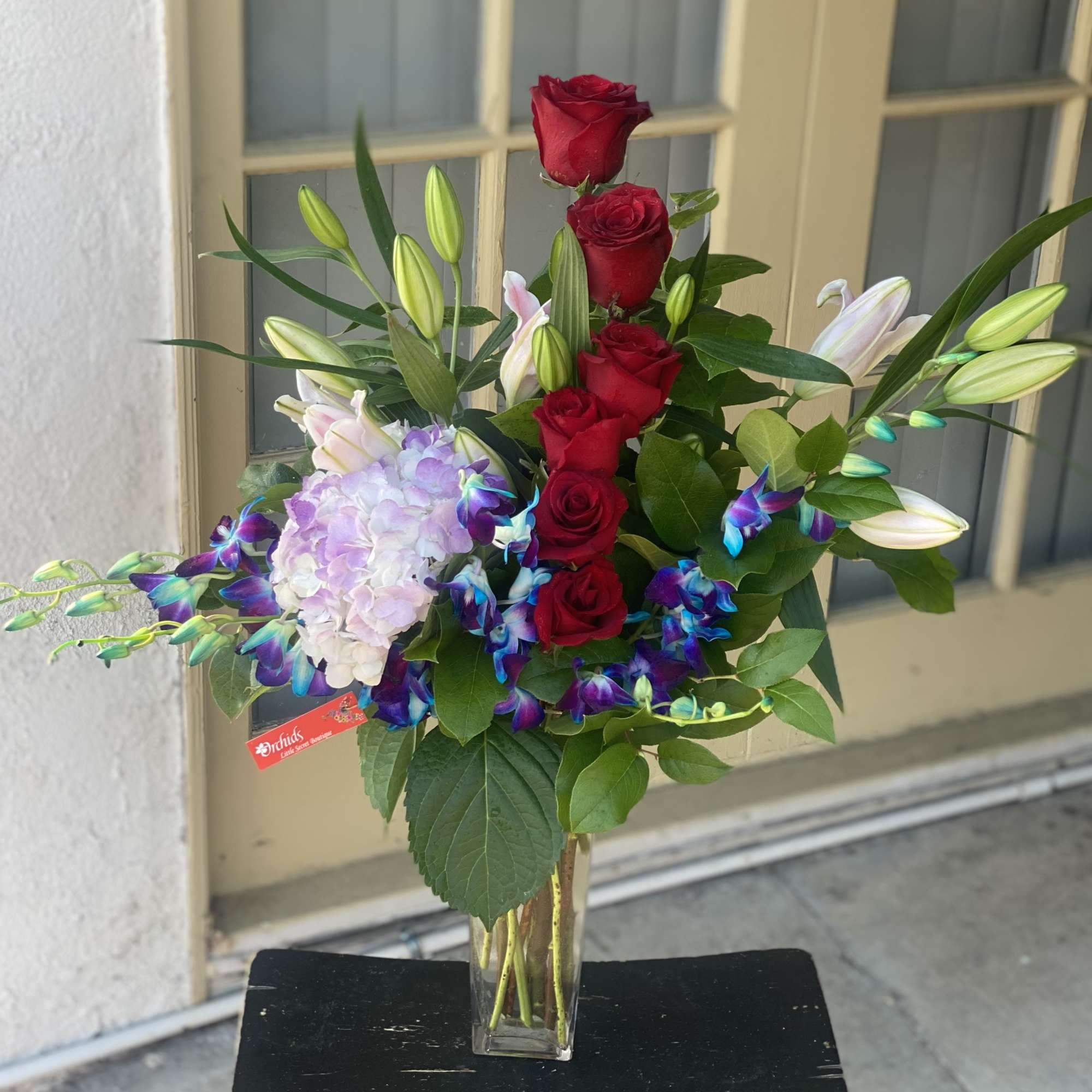 Red roses and lilies in a clear glass vase with purple orchids