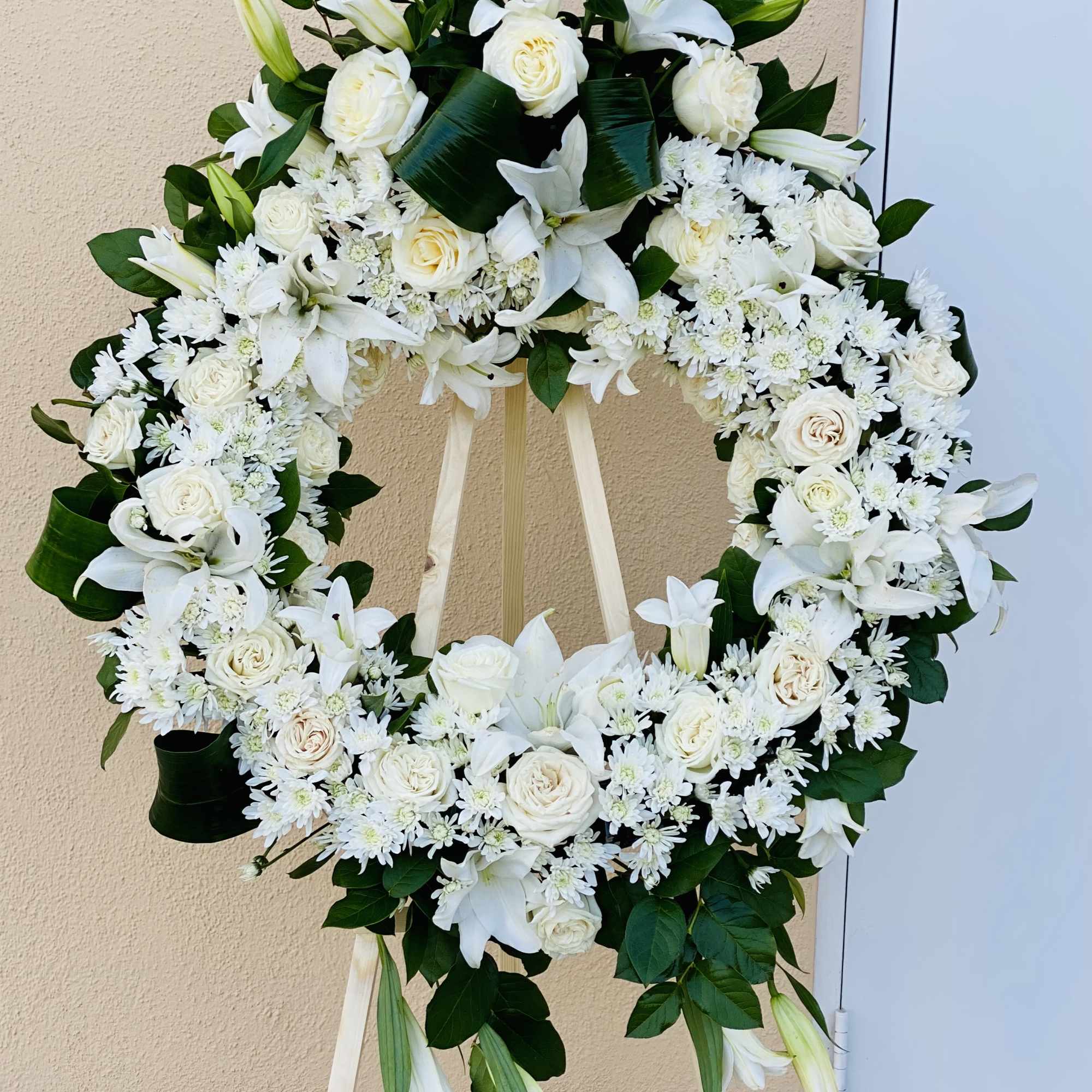 White floral wreath on a standing easel with lilies and roses