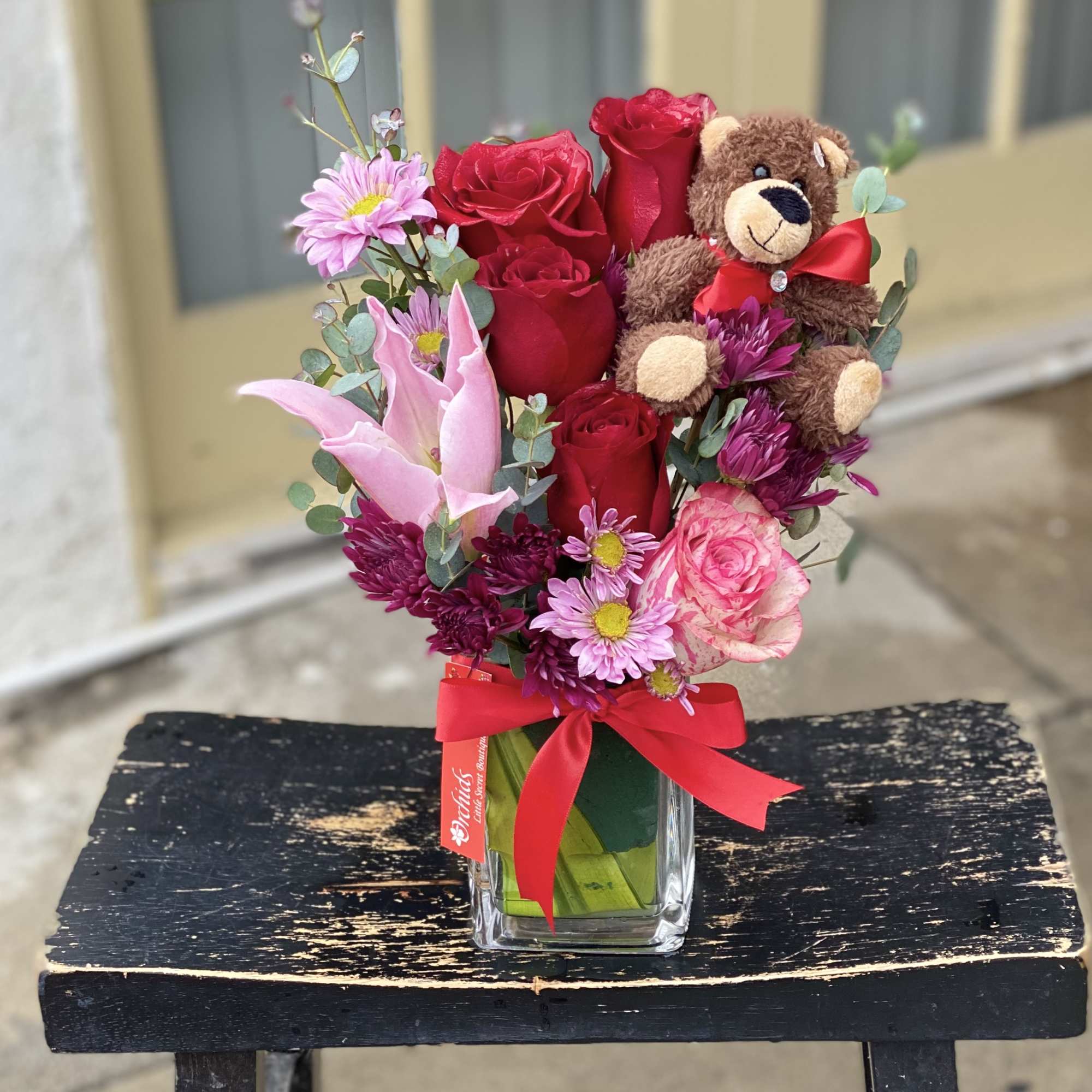 Bouquet of red and pink flowers with a teddy bear in a glass vase
